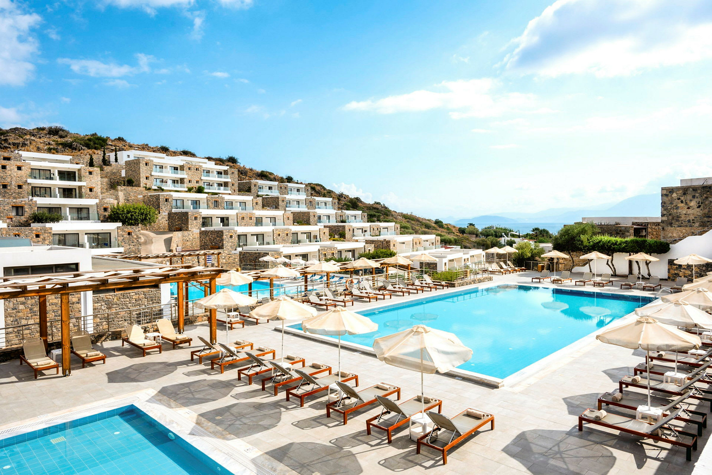 Billede af hotel med flere bygninger, swimmingpool og liggestole udendørs. (AI-genereret tekst)