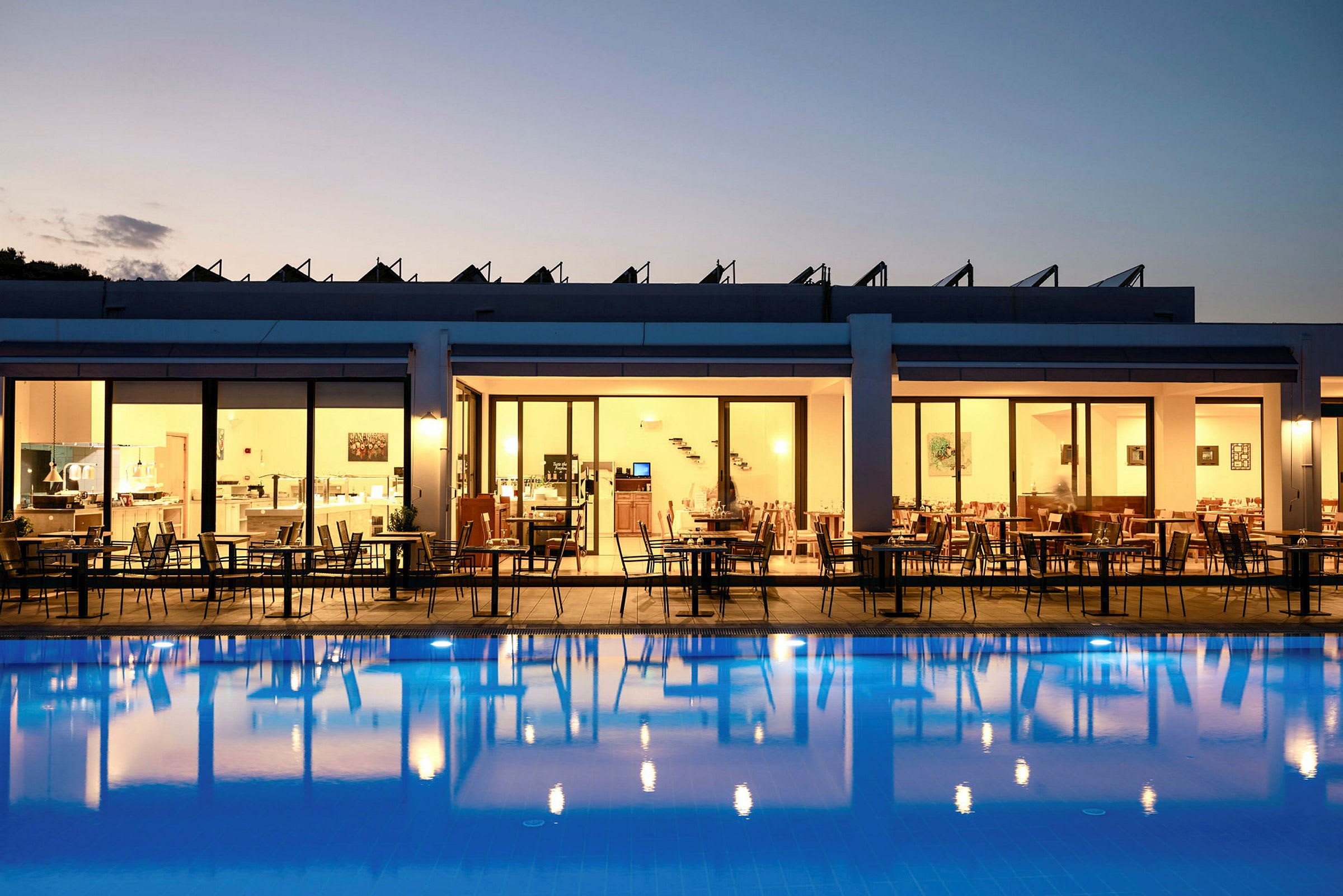 Hotelrestaurant med udendørs servering om aftenen, med udsigt til en belyst pool. (AI-genereret tekst)