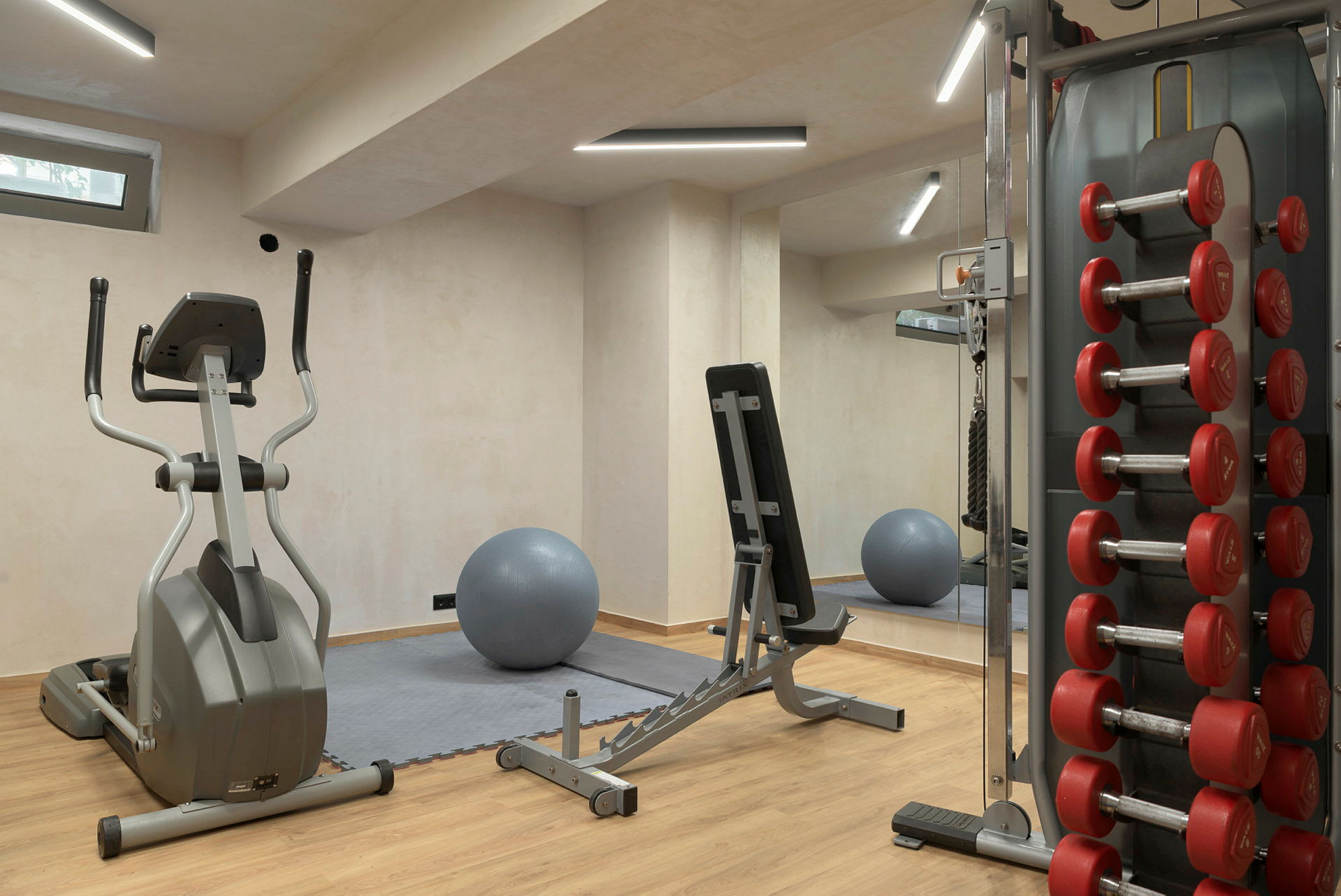 Fitnesslokale med træningsmaskiner, bænk, håndvægte og en grå træningsbold. (AI-genereret tekst)