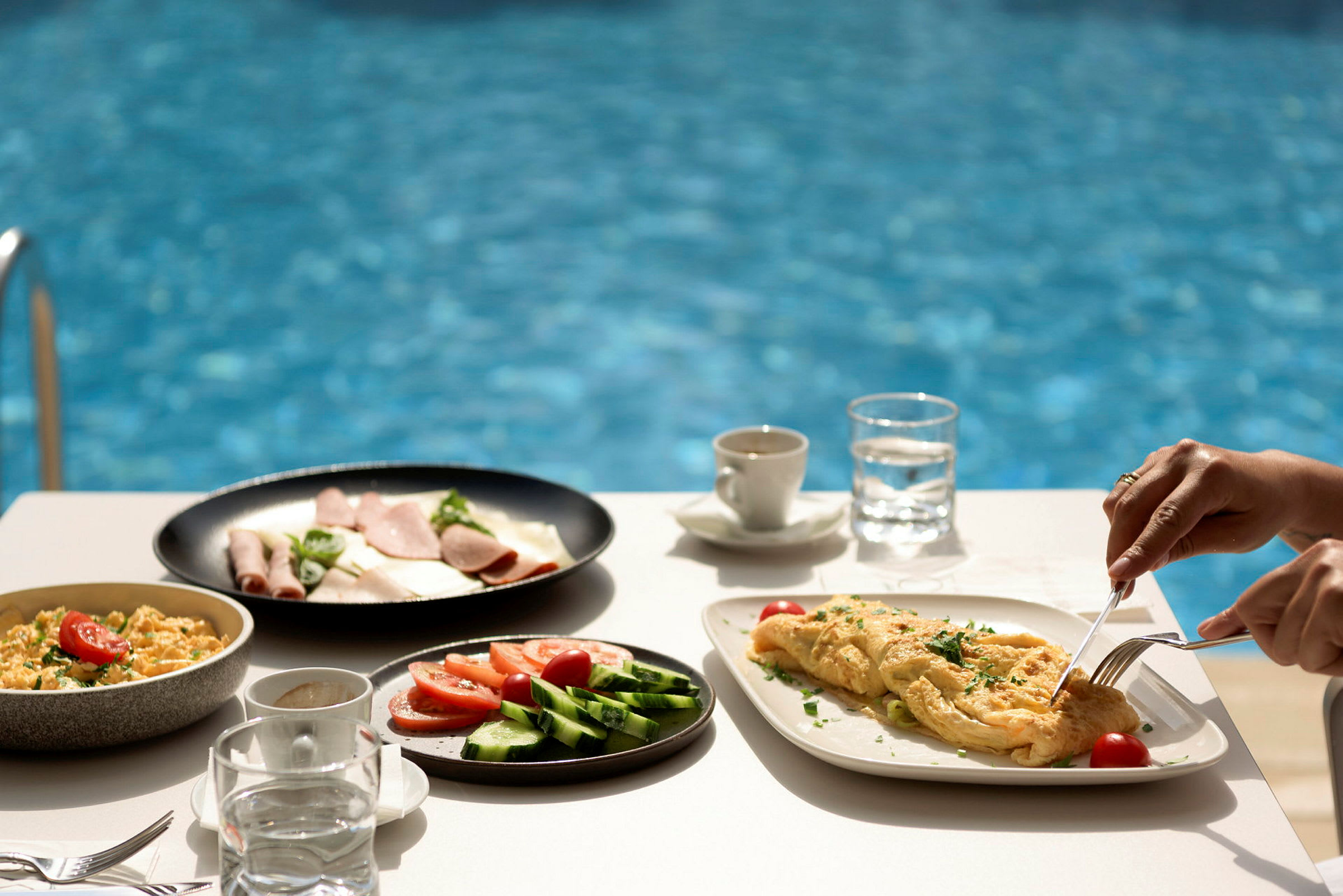 Morgenmad ved en pool, med omelet og grøntsager på tallerken. (AI-genereret tekst)