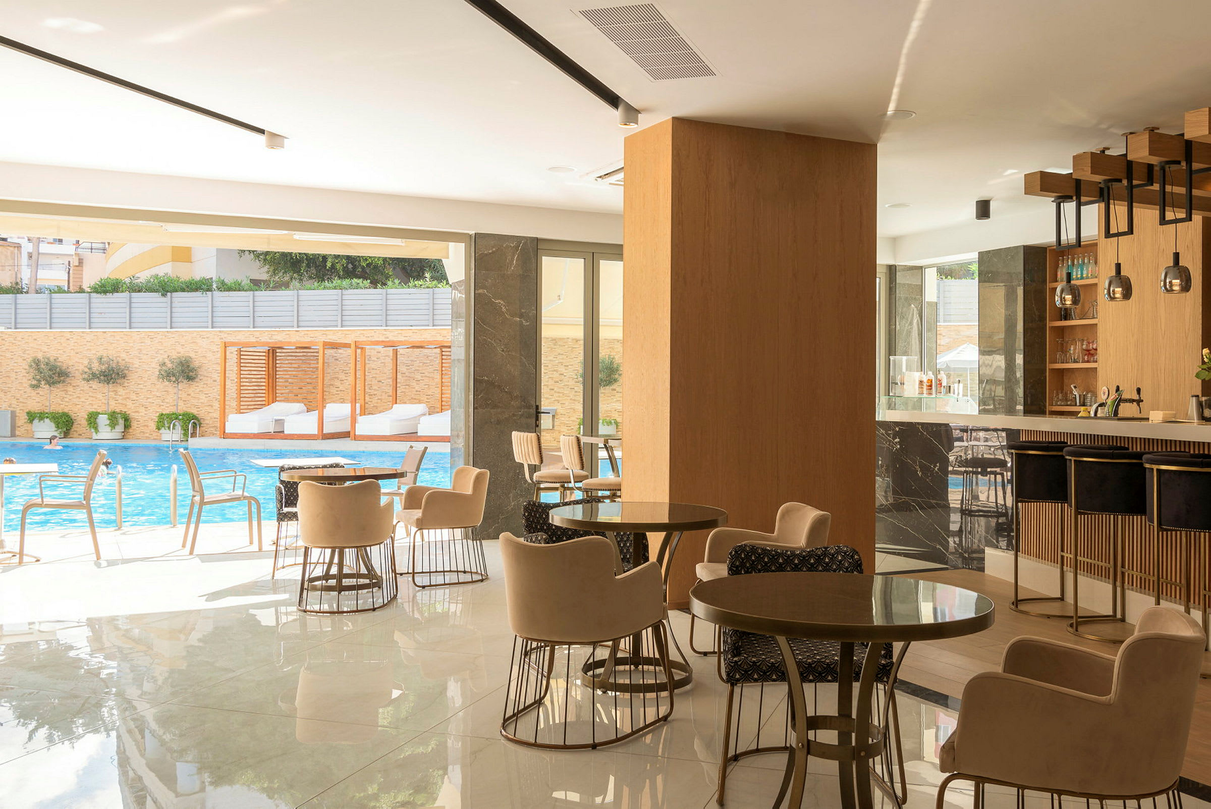 Et moderne caféområde med siddegrupper, en bar og udsigt til en swimmingpool udenfor. (AI-genereret tekst)
