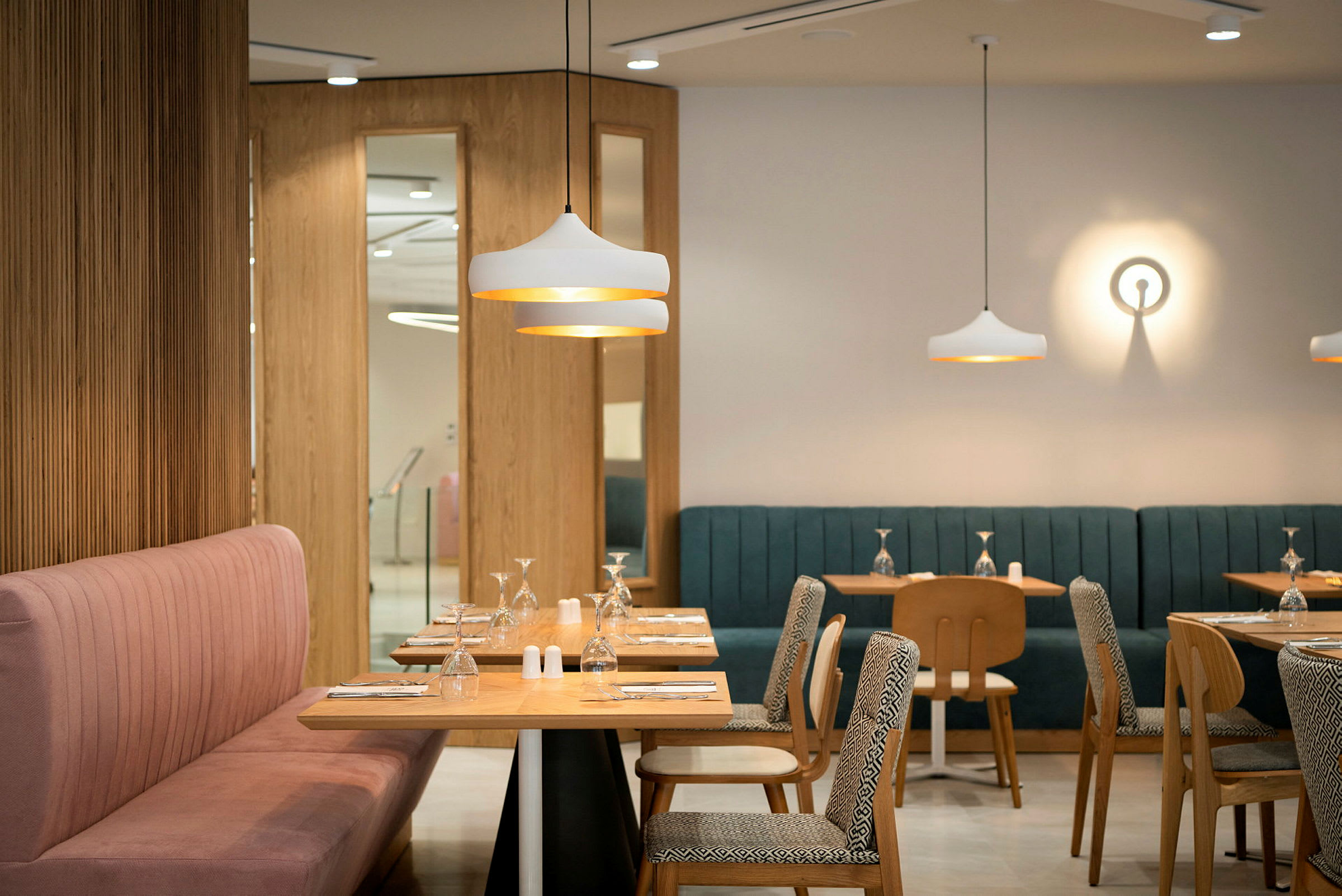 En moderne restaurant med borde og stole i træ, farverige polstrede sofaer og dekorative lampearmaturer. (AI-genereret tekst)
