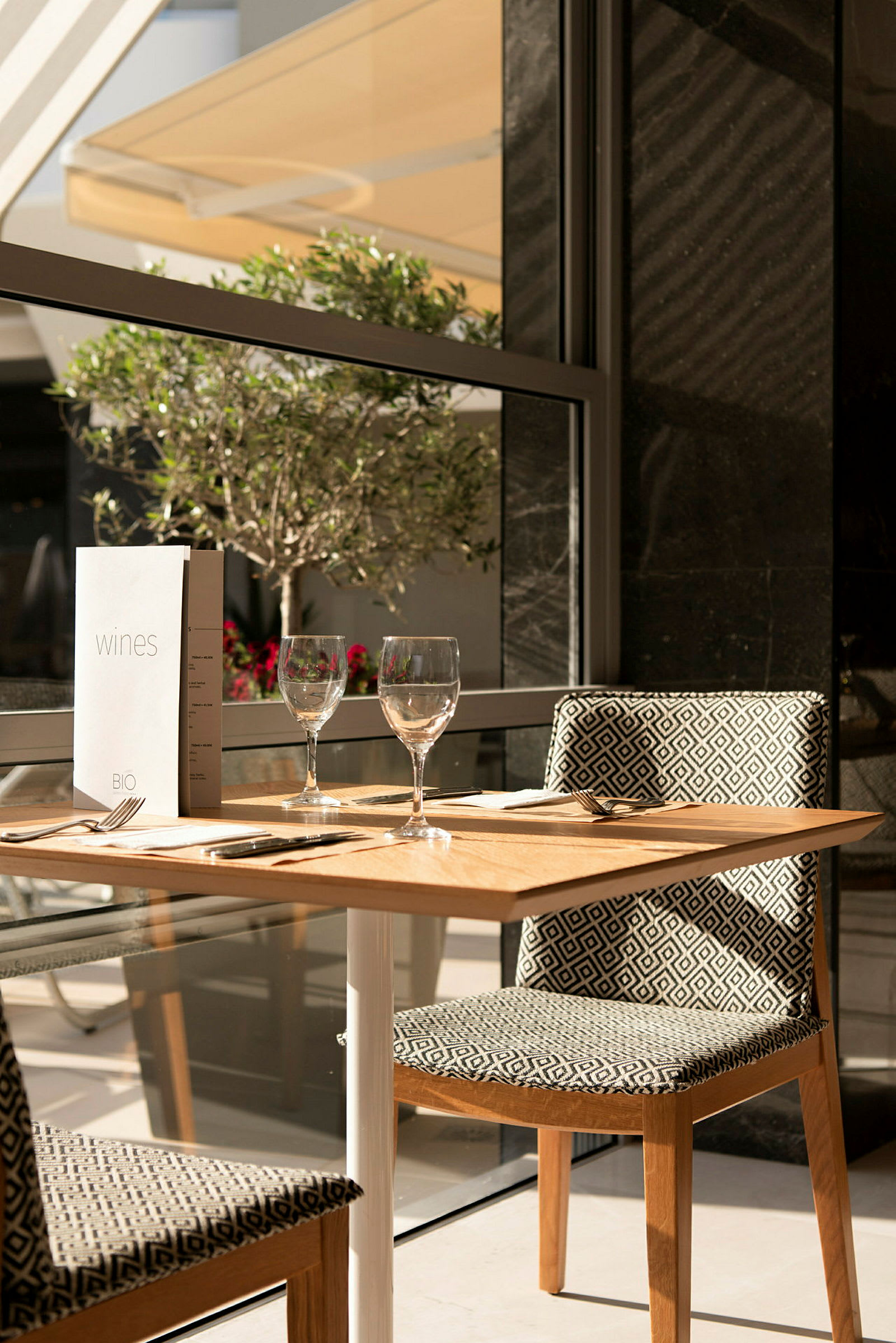 Et dækket bord med to glas og en menu ved vinduet. (AI-genereret tekst)
