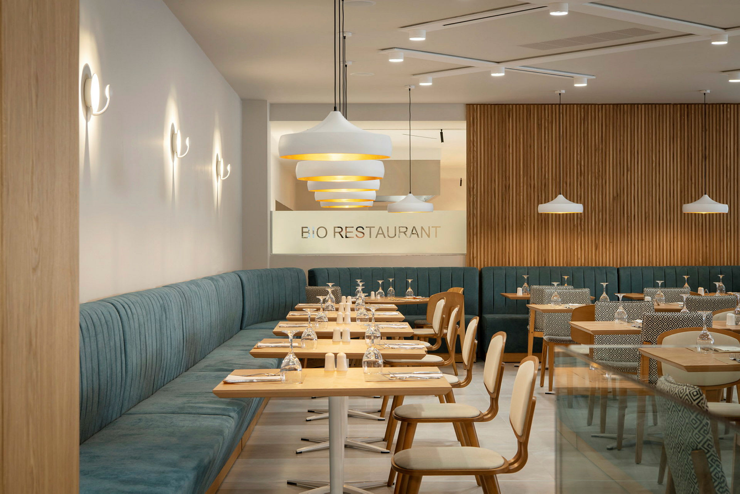 Moderne restaurant med træborde og polstrede siddepladser. Glas og tallerkener er arrangeret på bordene. (AI-genereret tekst)