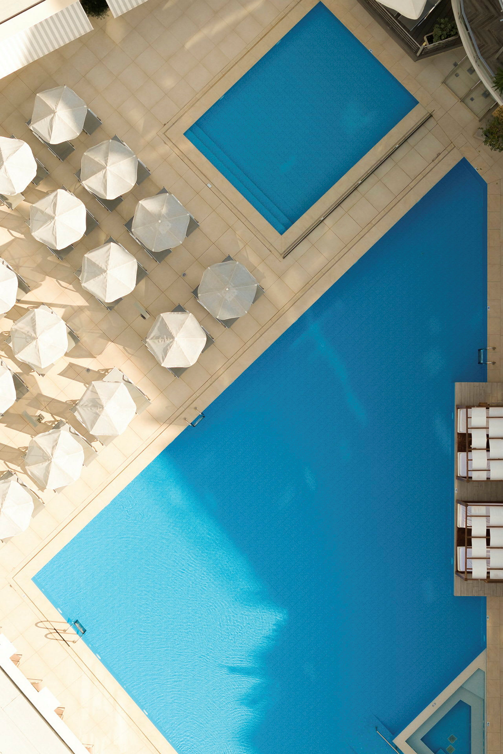 Luftfoto af en swimmingpool omgivet af parasoller og liggestole. (AI-genereret tekst)
