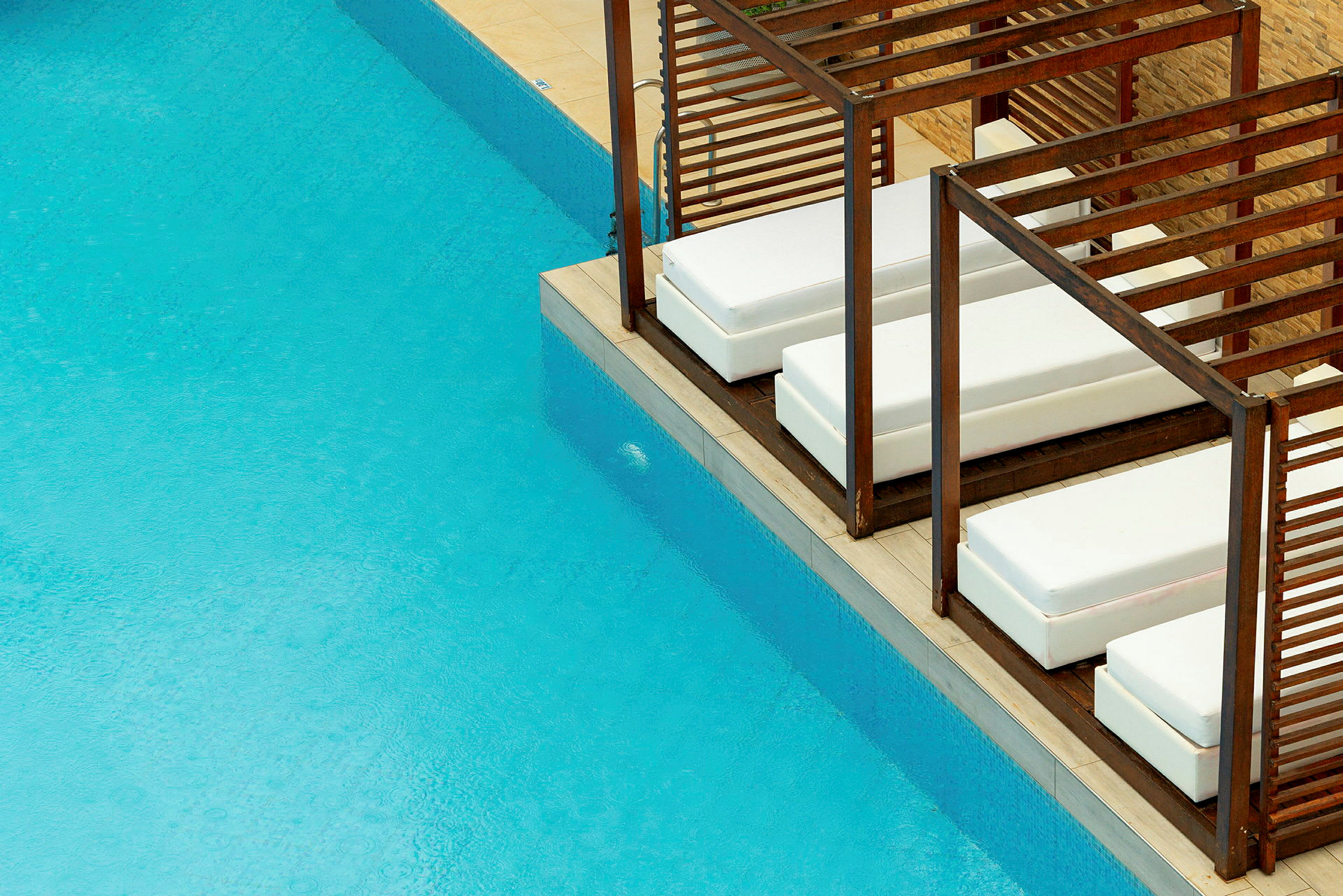 Lounge møbler med hvide puder ved en pool med blåt vand. (AI-genereret tekst)