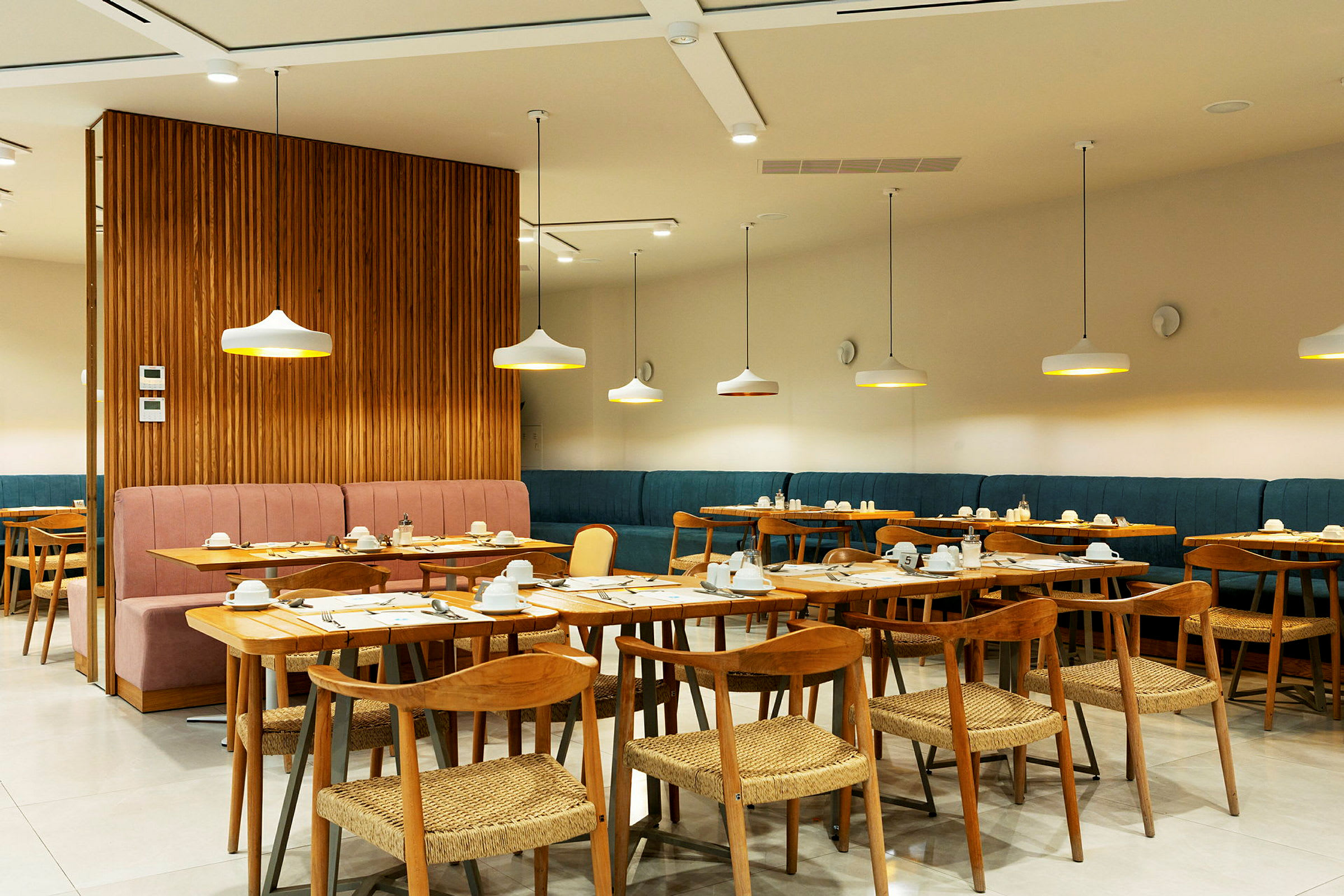 En moderne indendørs restaurant med borde og stole i træ samt stilfuldt placerede loftslamper. (AI-genereret tekst)