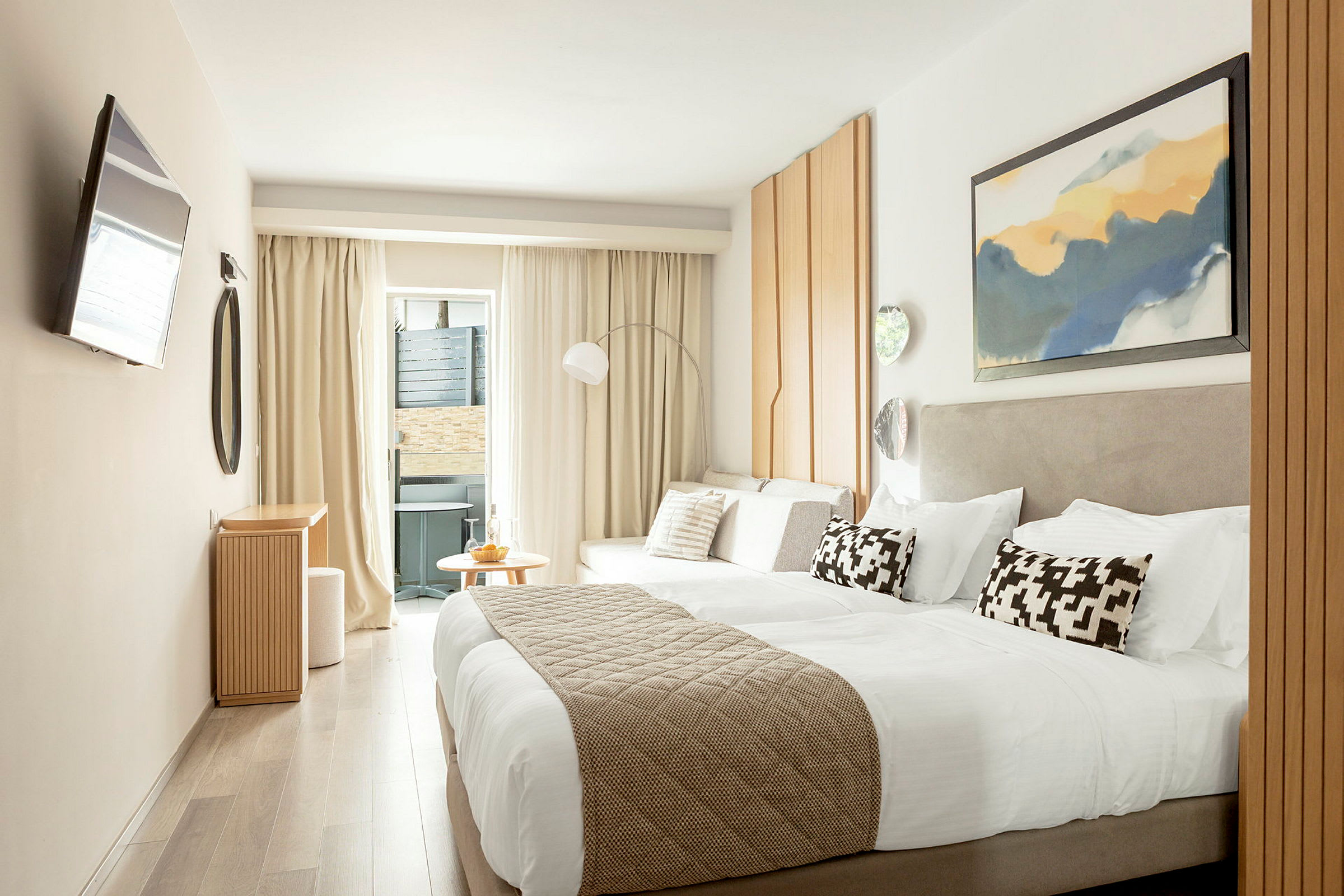 Et moderne hotelværelse med en dobbeltseng, lyse møbler og dekorationer samt en lille siddegruppe tæt ved et vindue. (AI-genereret tekst)