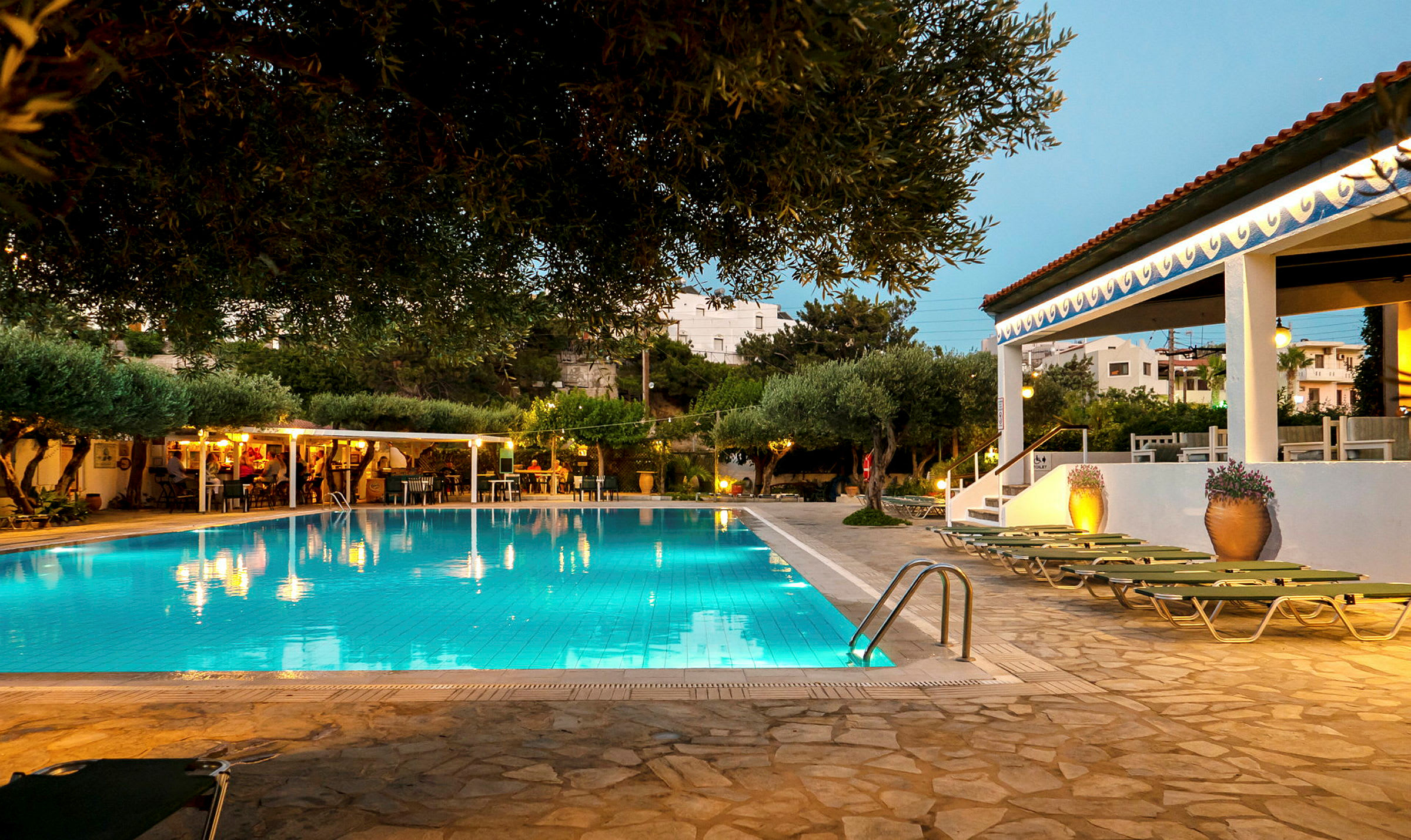 Udendørs swimmingpool ved et hotel med liggestole og grønne omgivelser. (AI-genereret tekst)