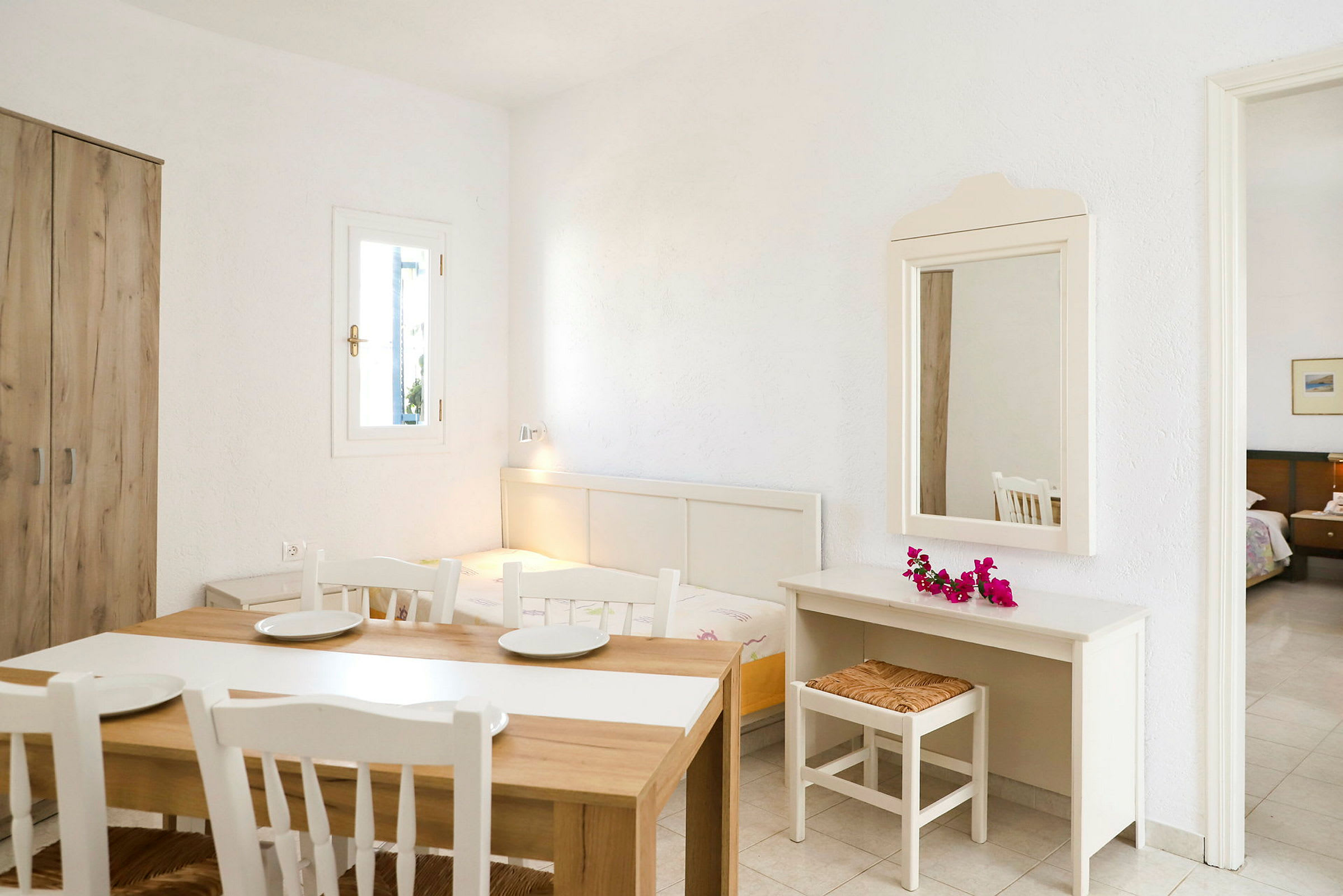 Et lyst værelse med bord, stole, spejl, skrivebord og en seng. (AI-genereret tekst)