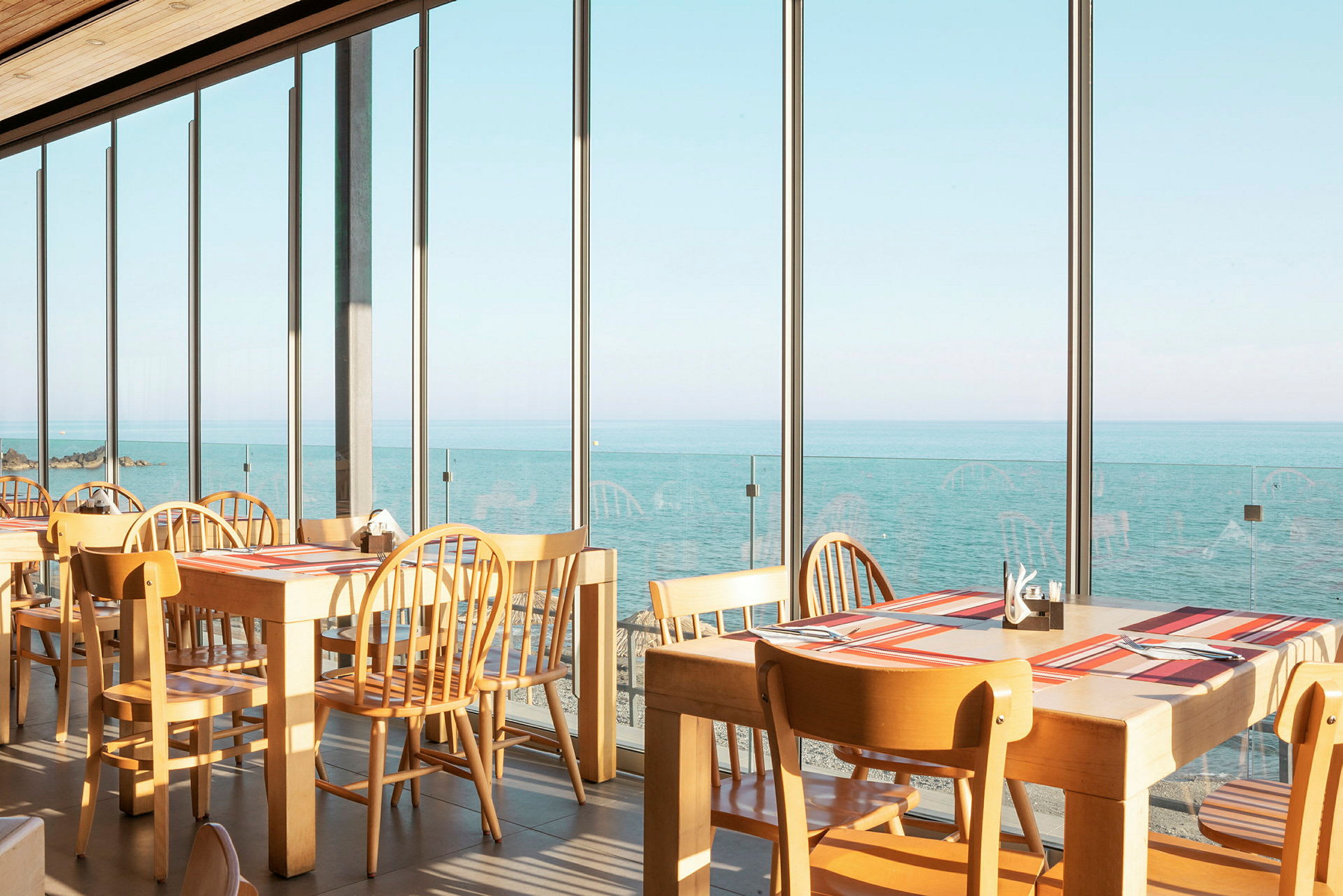 Restaurant med borde og stole ved store vinduer med udsigt over havet. (AI-genereret tekst)