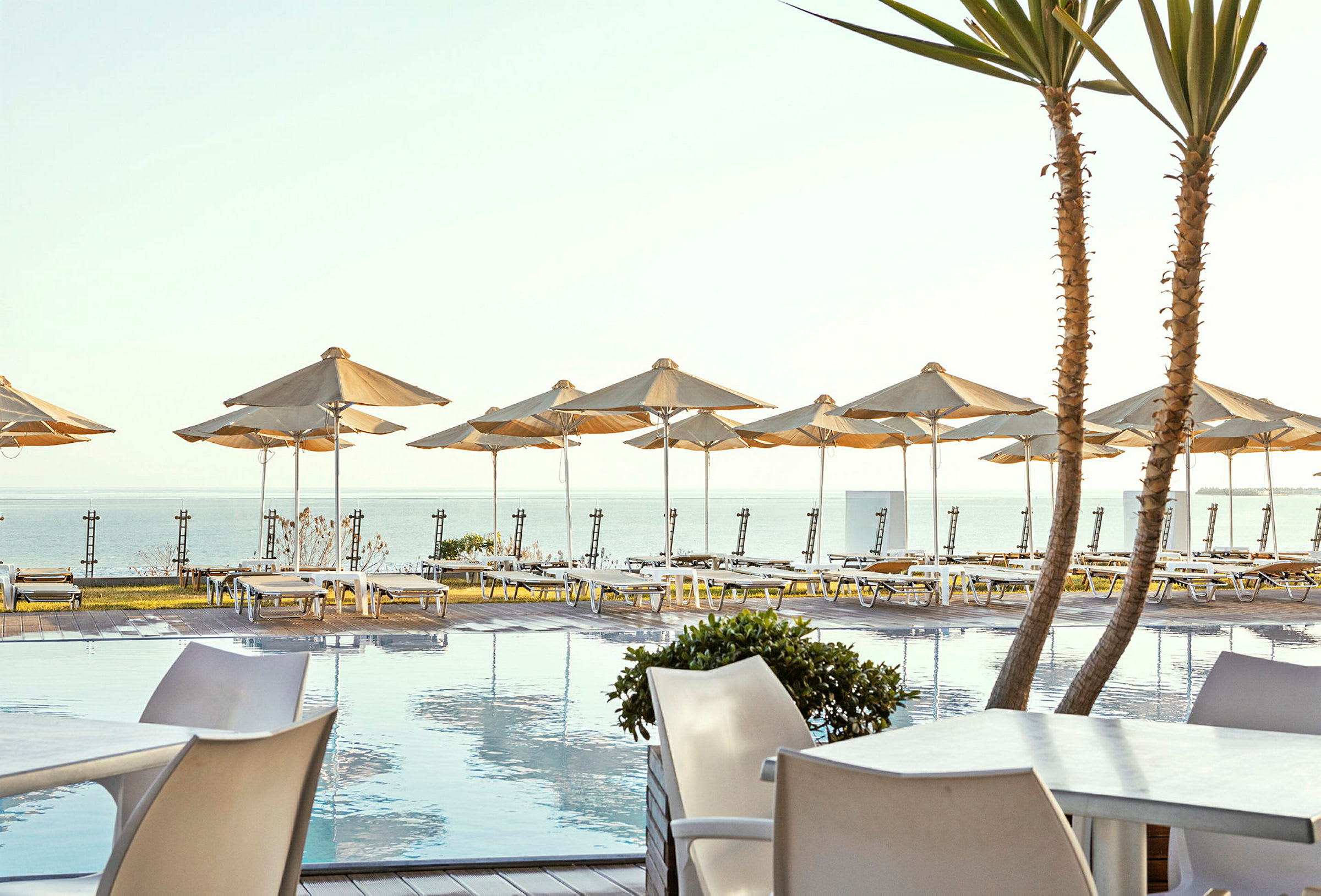 Solterrasse ved poolen med liggestole og parasoller ved havet. (AI-genereret tekst)