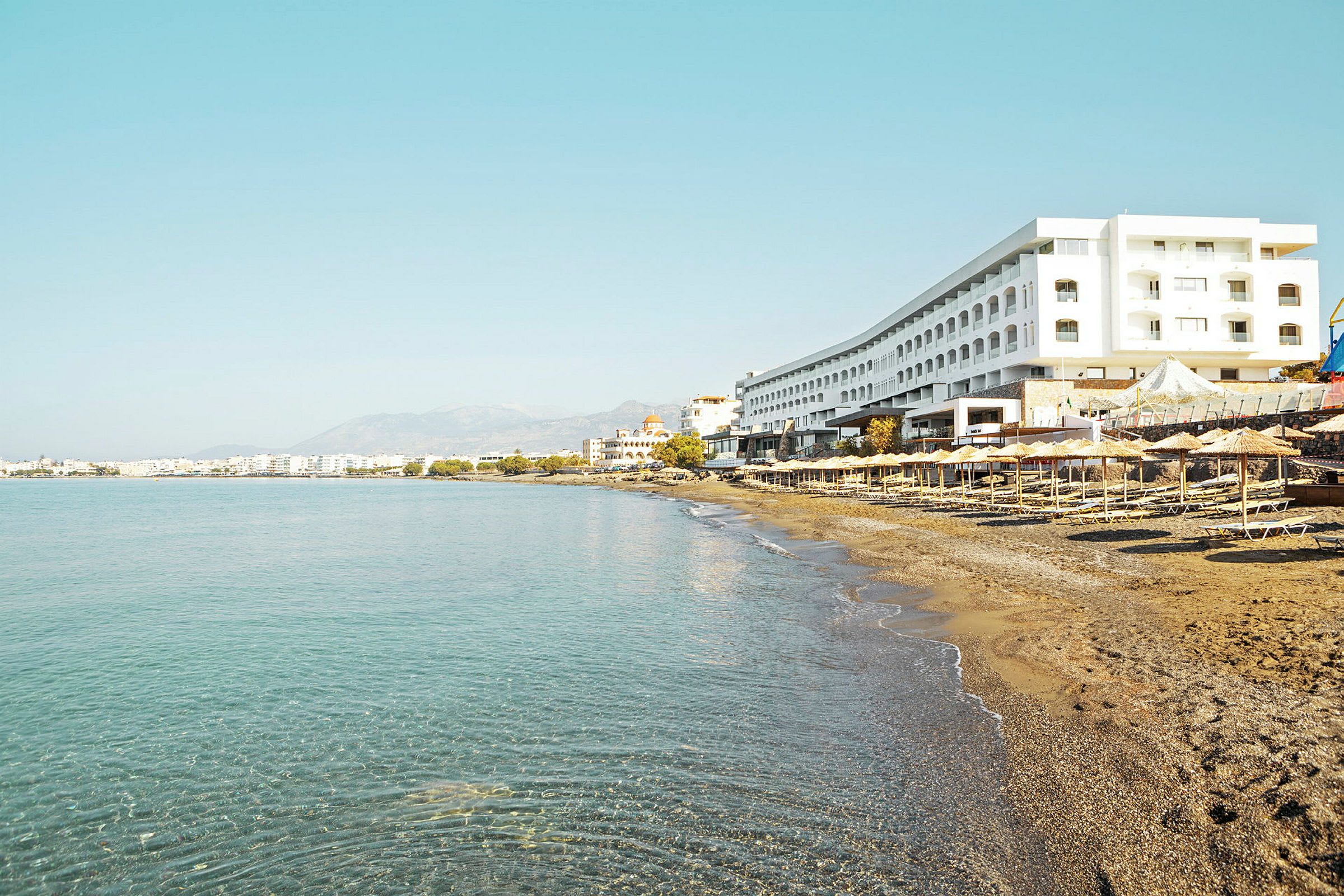 En strand med liggestole og parasoller ved foden af et stort hotel. (AI-genereret tekst)
