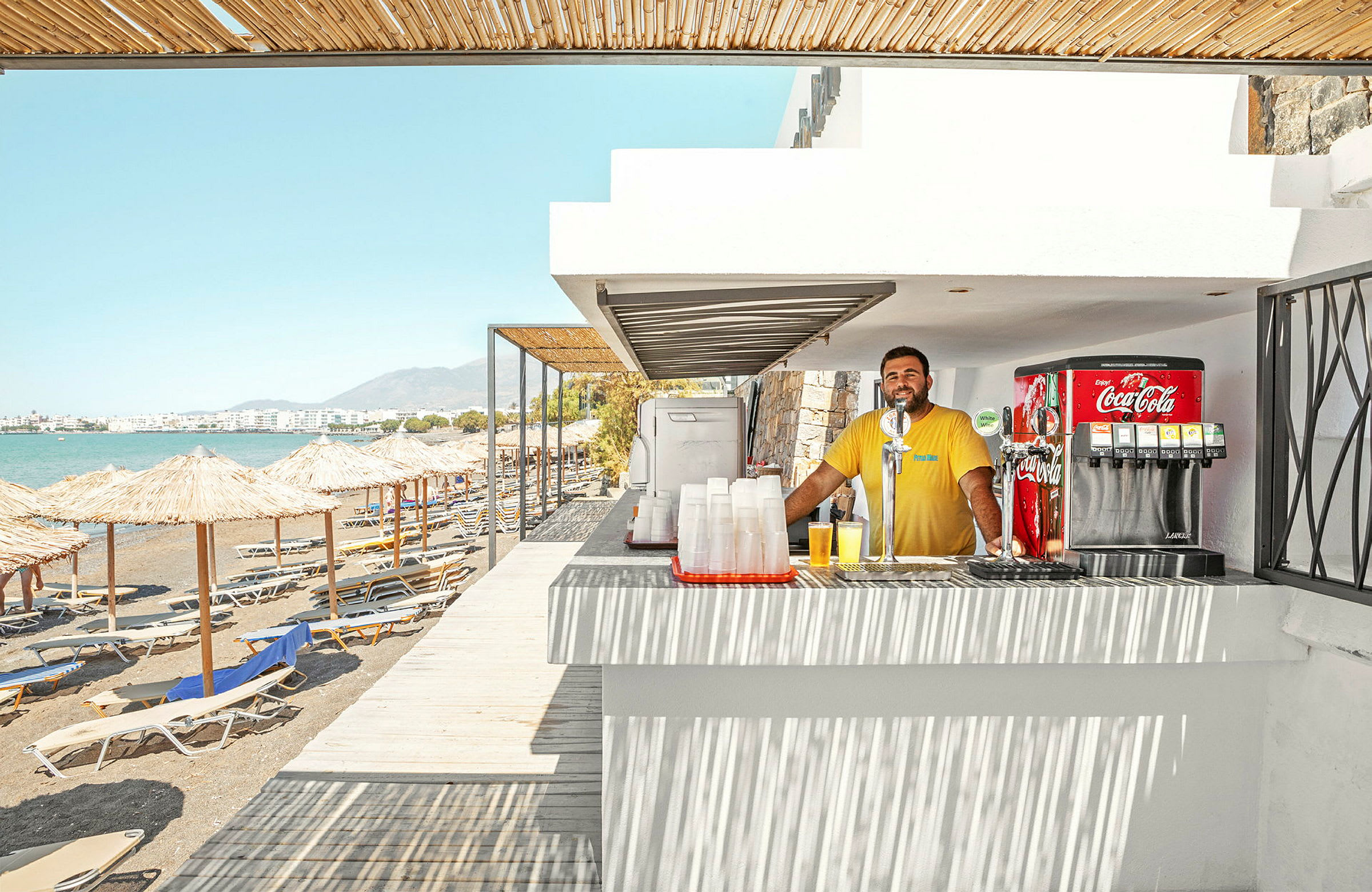 En strandbar ved havet med liggestole og parasoller på stranden. (AI-genereret tekst)