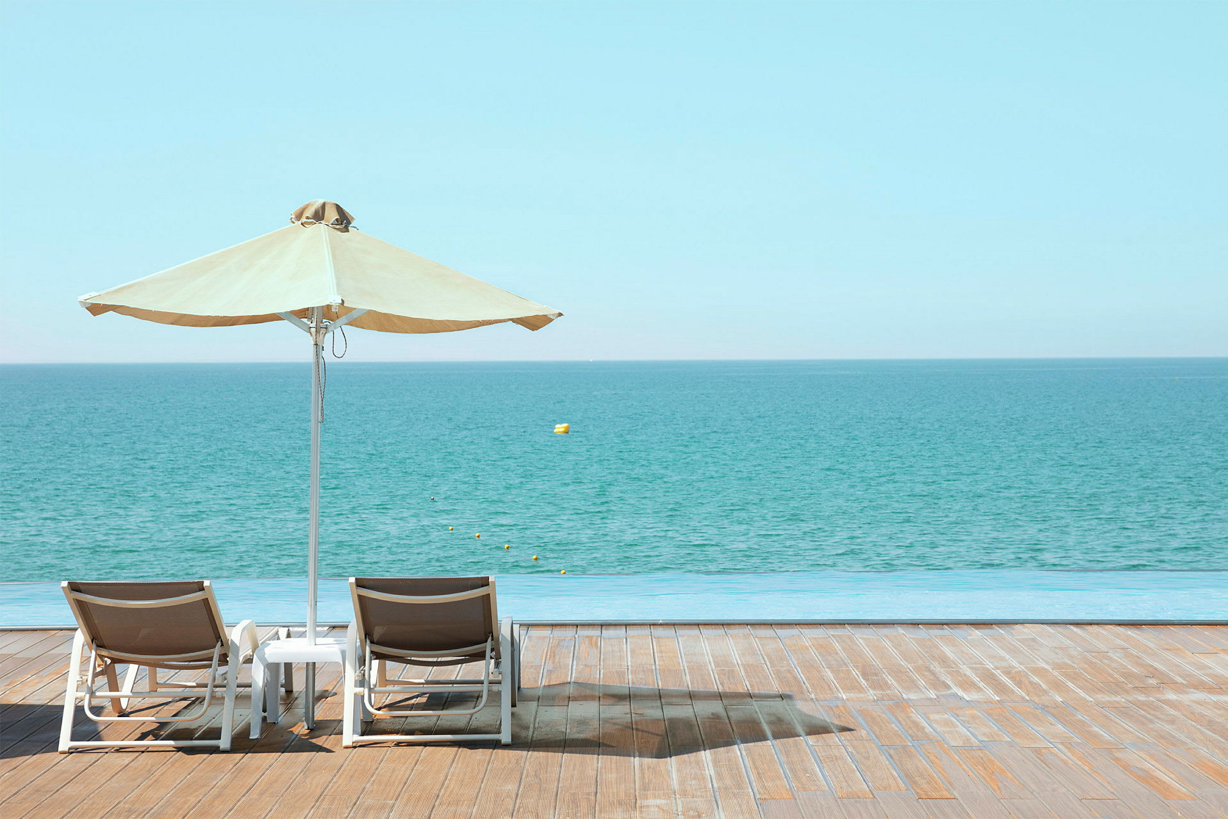 To solsenge står på en træterrasse ved havet under en parasol. (AI-genereret tekst)