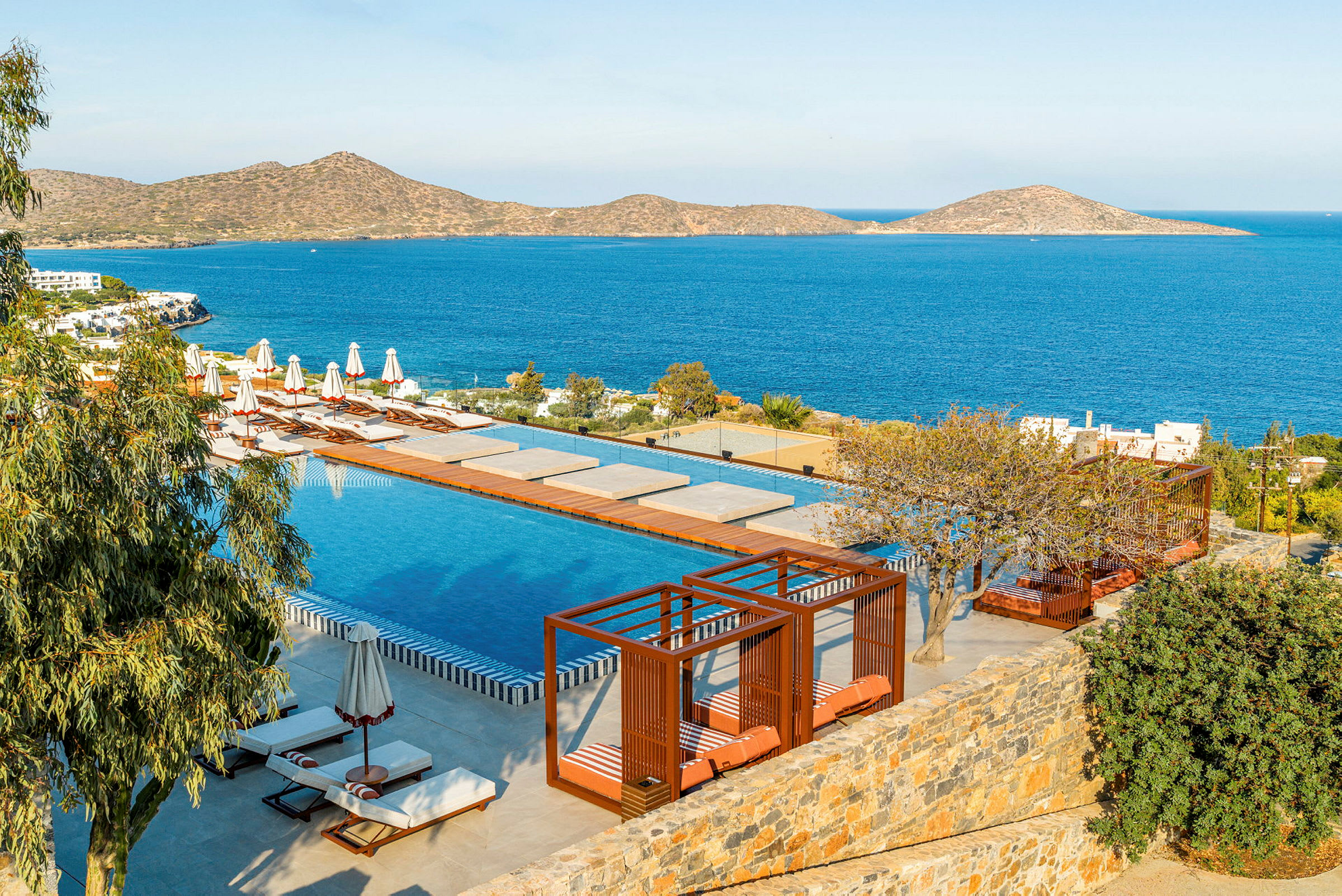 En luksuriøs pool med liggestole og cabanas ved havet på en solrig dag. (AI-genereret tekst)