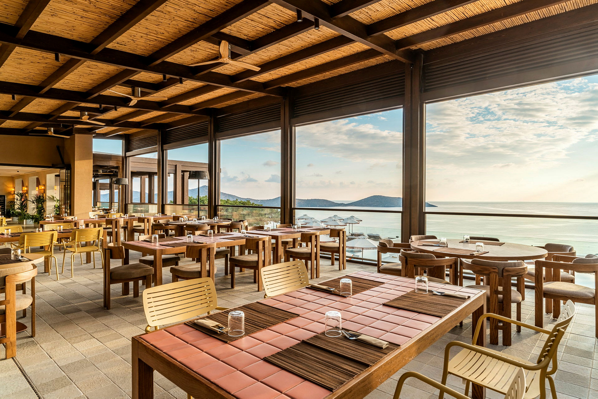 En åben og lys restaurant med træborde og stole, med udsigt over havet og horisonten. (AI-genereret tekst)
