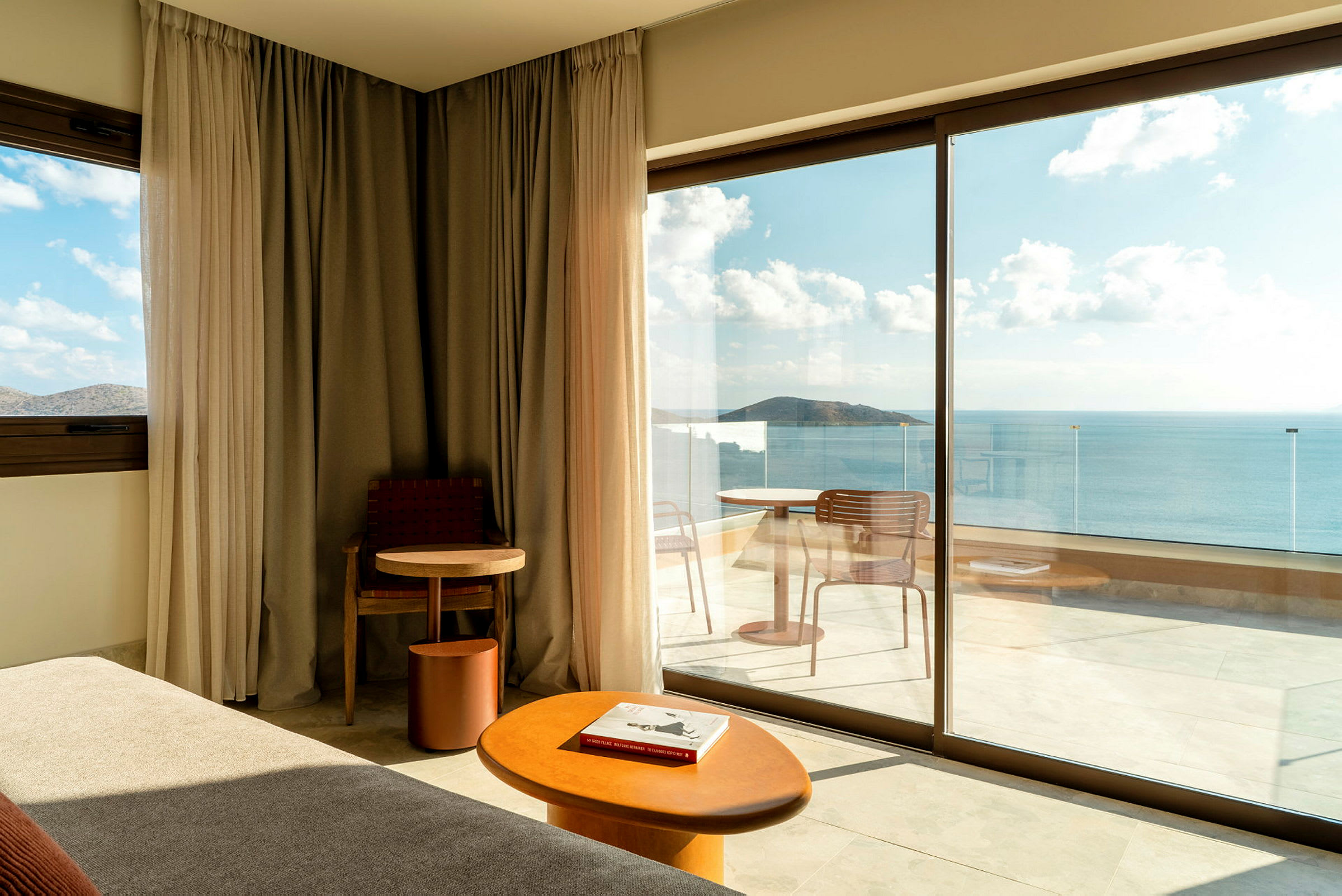 Moderne hotelværelse med store glasdøre, der fører ud til en altan med havudsigt. (AI-genereret tekst)