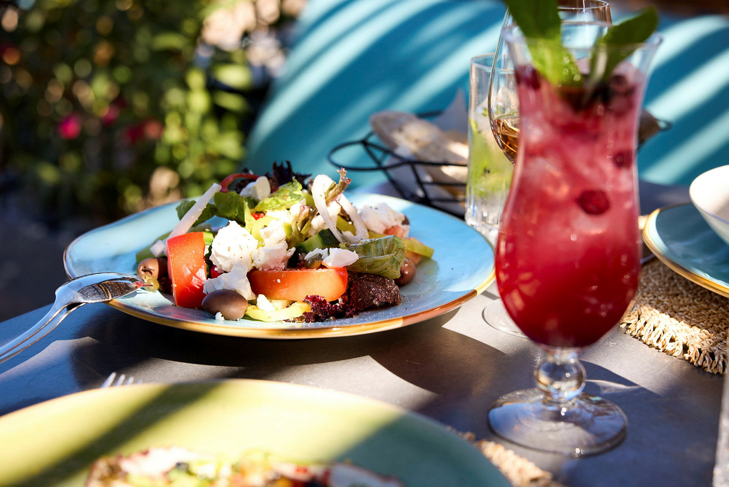 En tallerken med salat og en rød drink på et bord udendørs. (AI-genereret tekst)