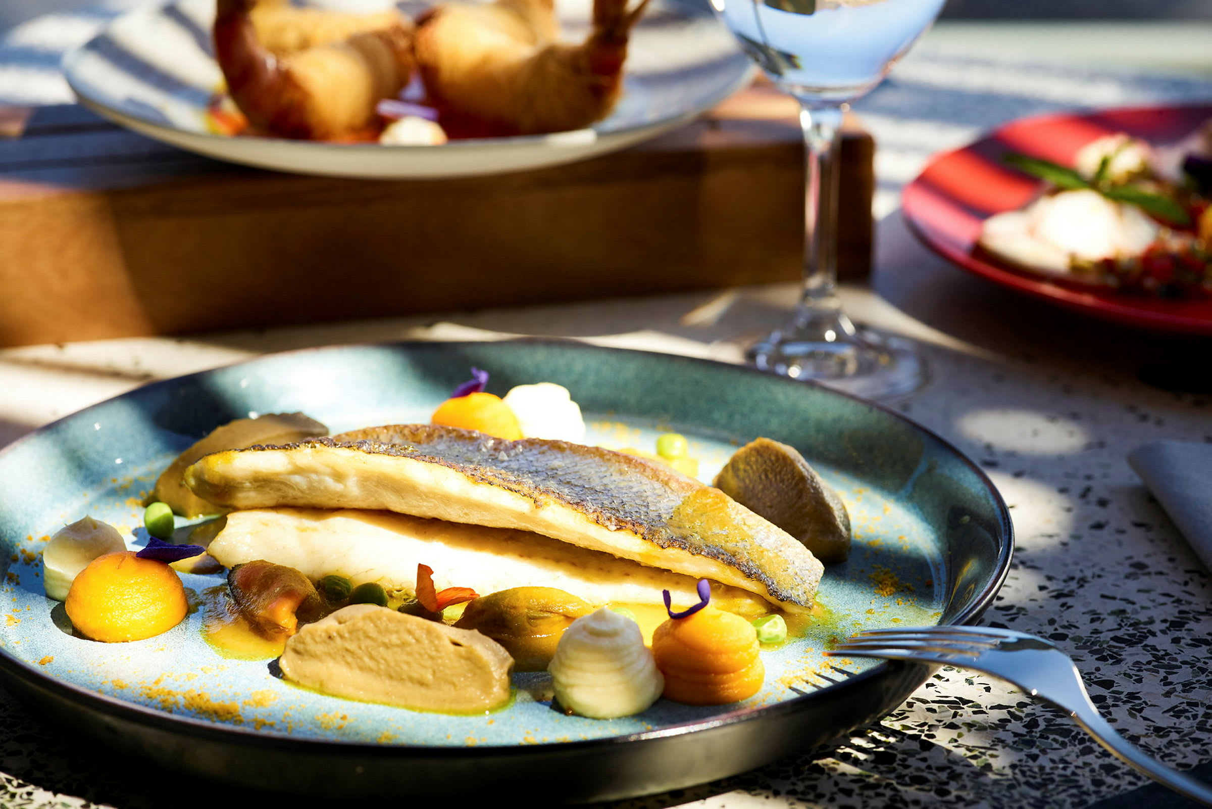 En tallerken med en elegant anrettet fiskeret, omgivet af grøntsager og saucer. (AI-genereret tekst)