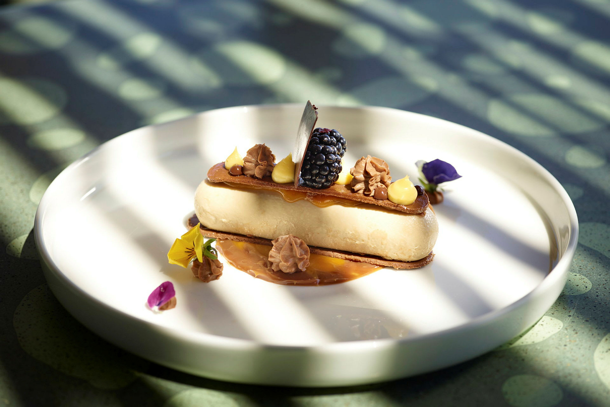 Dessert serveret på en hvid tallerken, dekoreret med fløde, bær og spiselige blomster. (AI-genereret tekst)