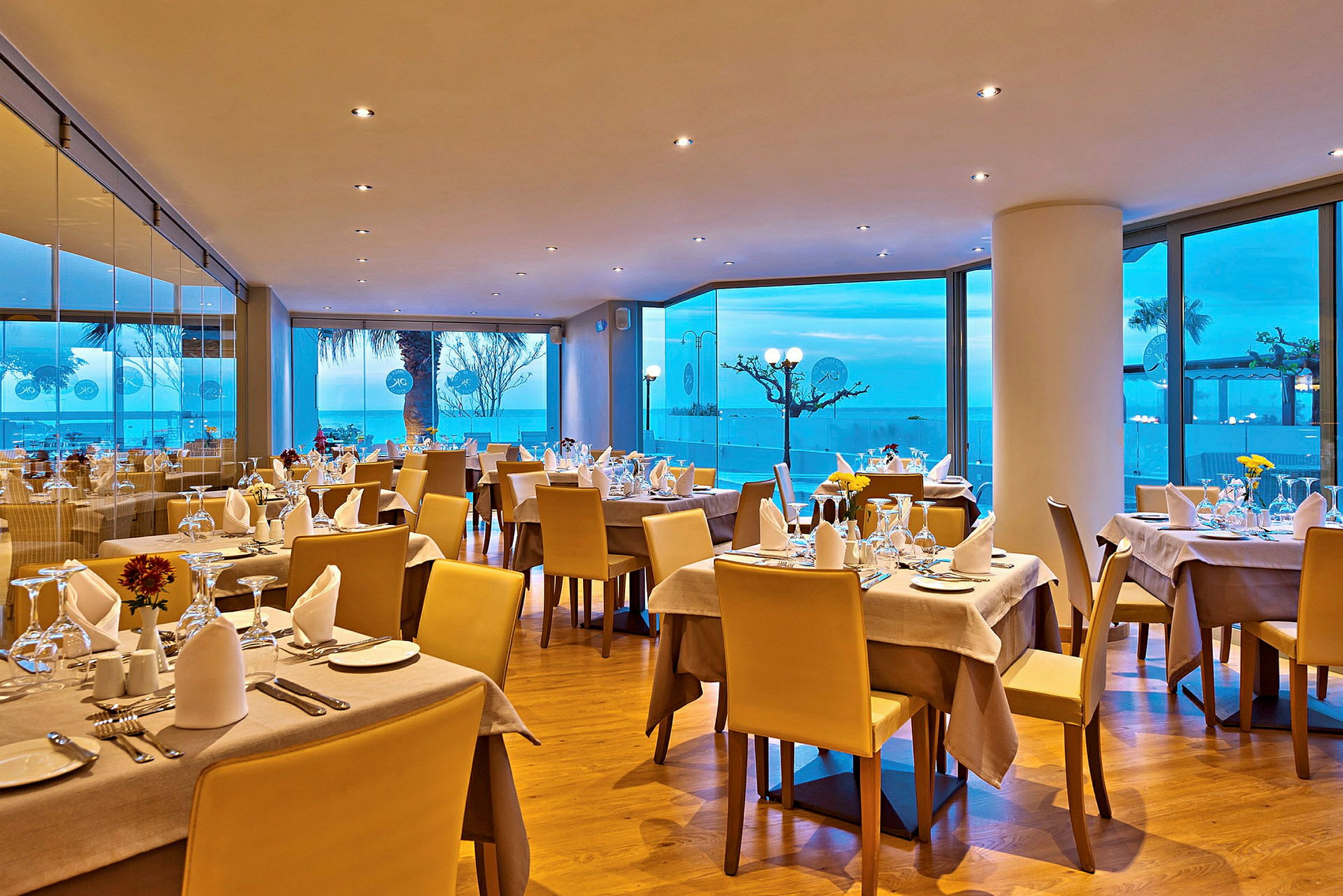 En elegant restaurant med dækkede borde og udsigt over havet gennem store vinduer. (AI-genereret tekst)