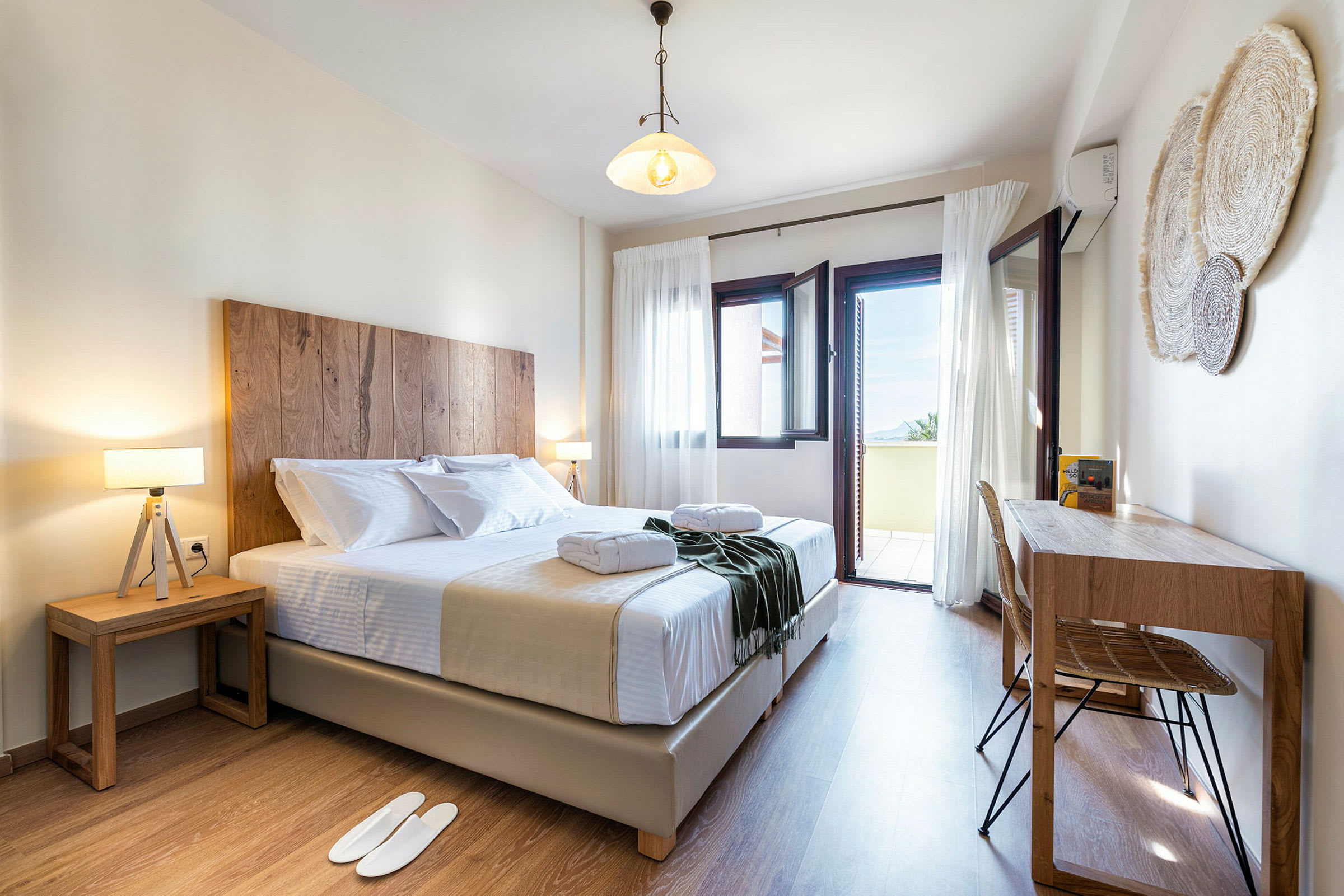 Et lyst og indbydende hotelværelse med en dobbeltseng, to natborde og et skrivebord. Vinduerne står åbne ud til en balkon med udsigt. (AI-genereret tekst)