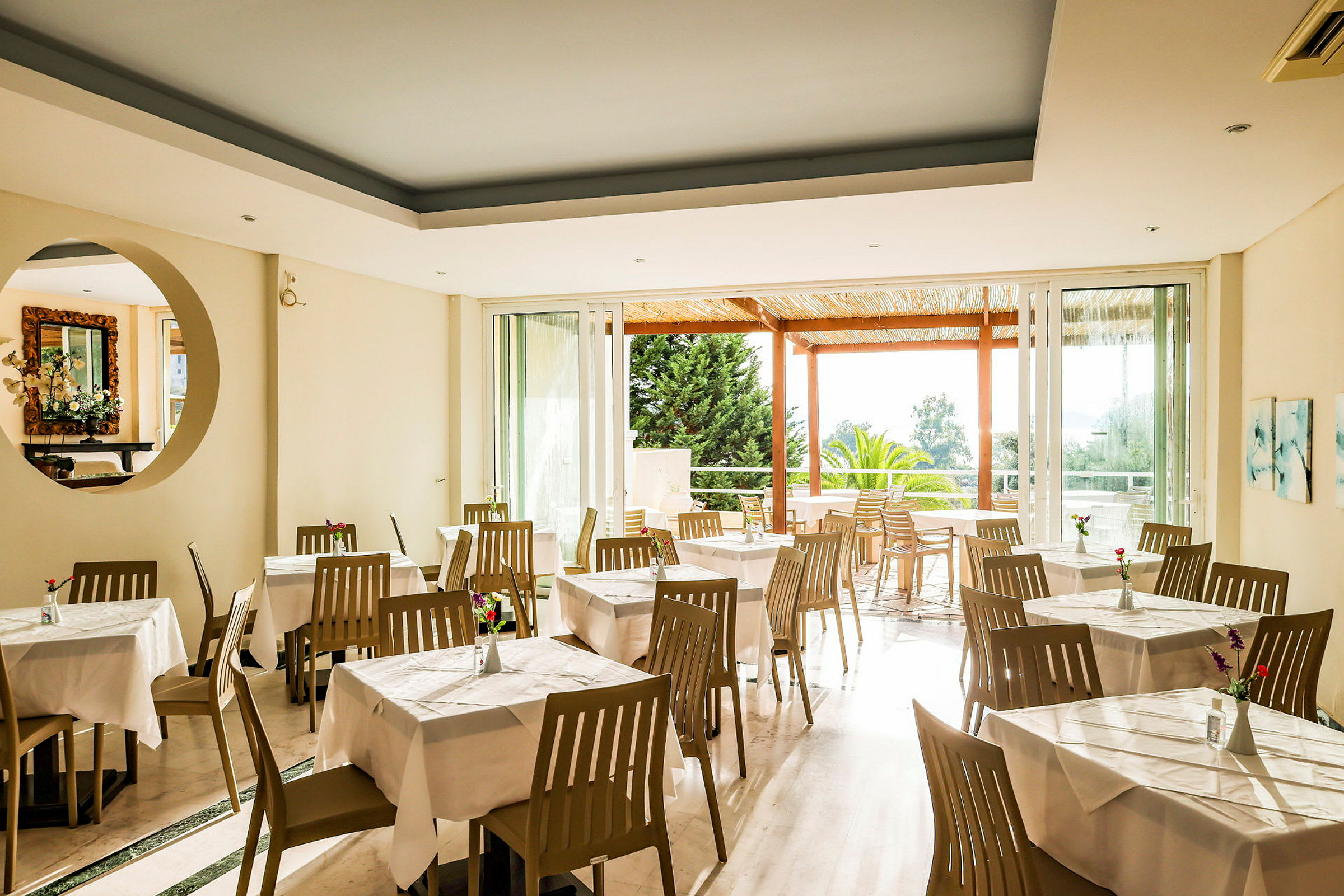 Restaurant med hvide duge og brune stole, lyse vægge og udsigt til en haveveranda. (AI-genereret tekst)