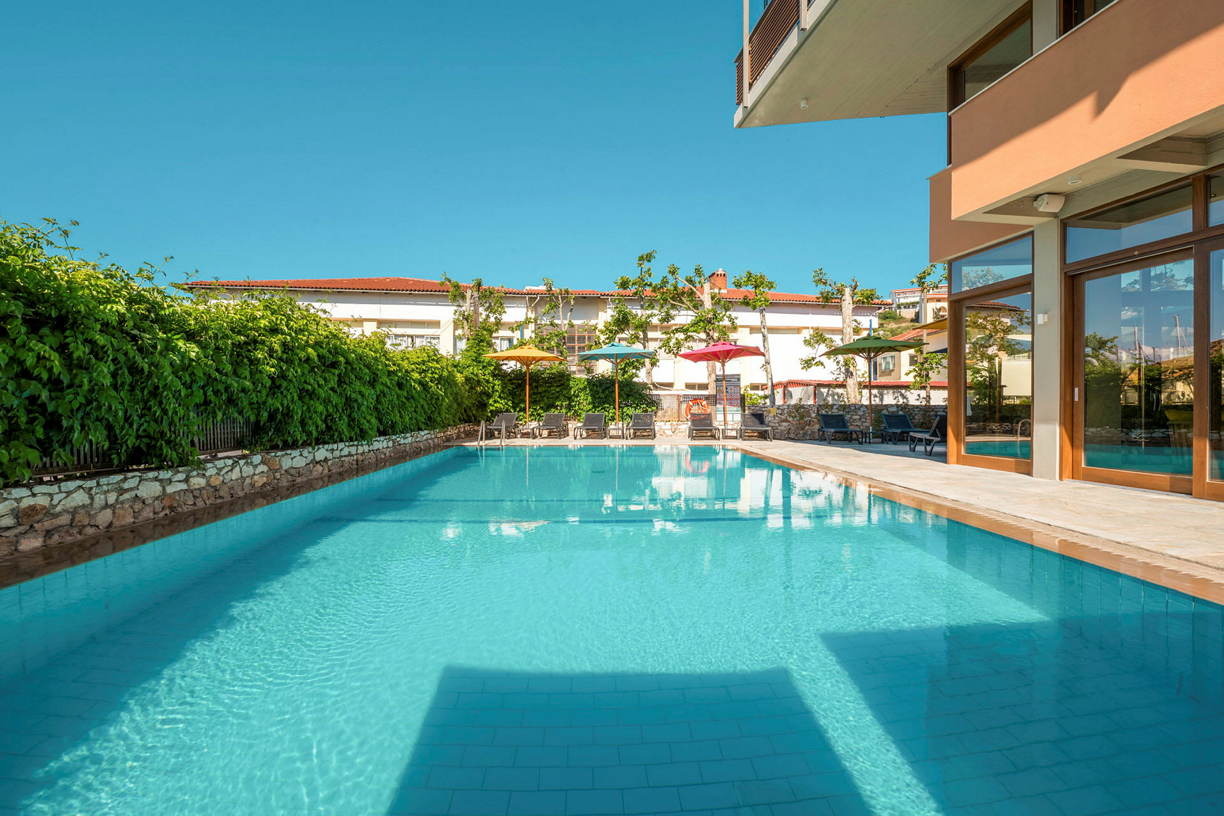 Udendørs swimmingpool omgivet af grønne områder og møblerede områder. (AI-genereret tekst)