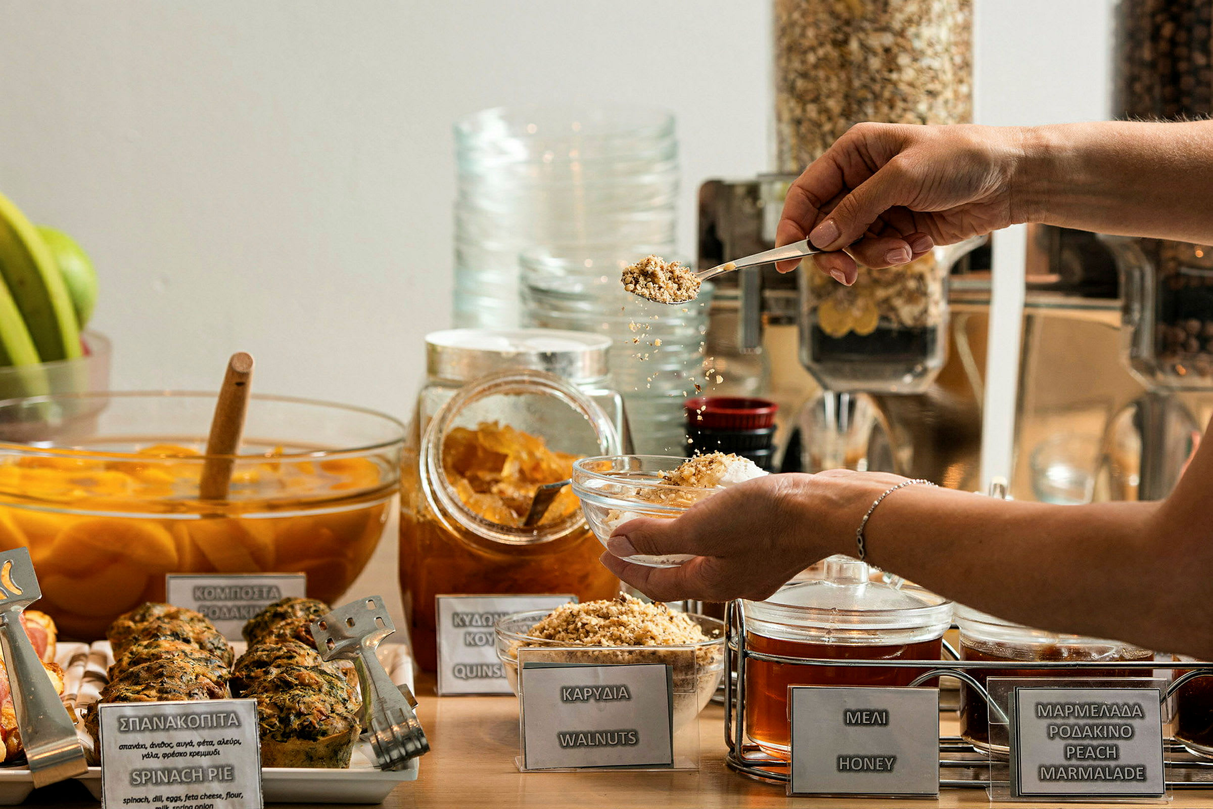 En morgenbuffet med forskellige valg som honning, nødder og marmelade. En person holder en skål og drysser nødder over den. (AI-genereret tekst)