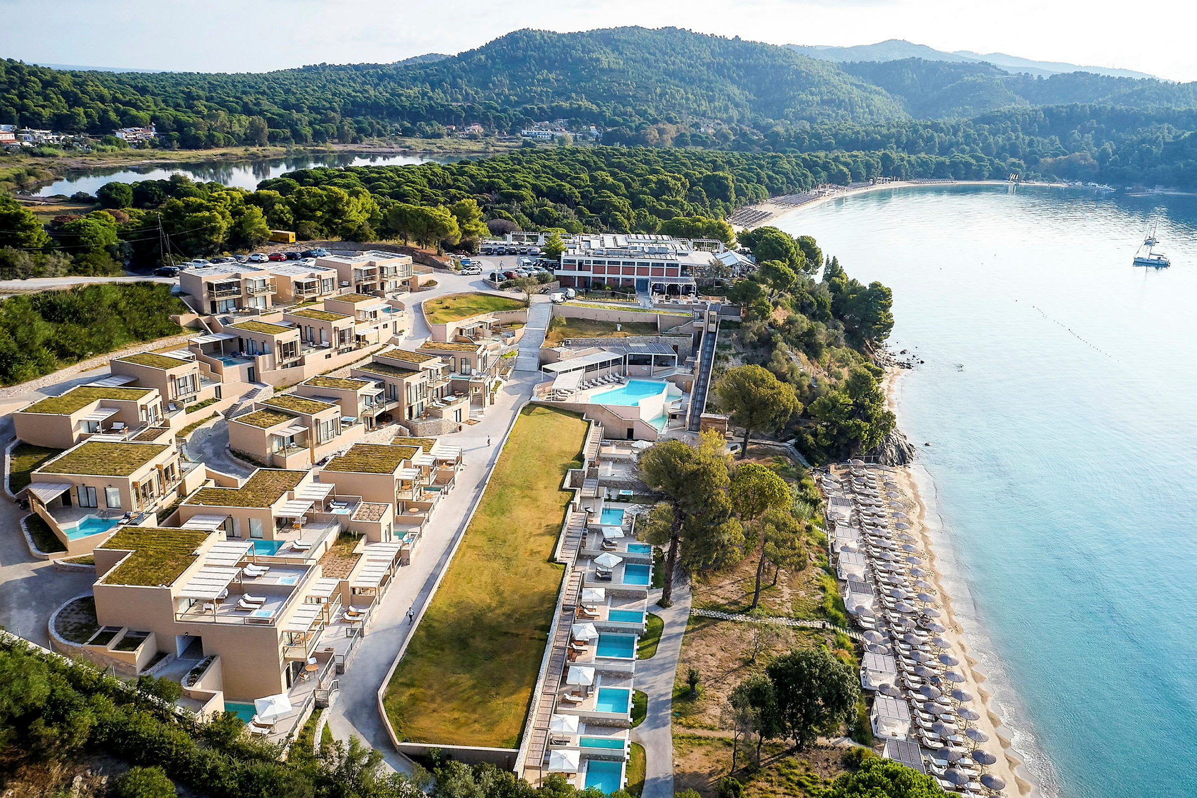 Luftfoto af et strandnært hotel med pools og liggestole. (AI-genereret tekst)