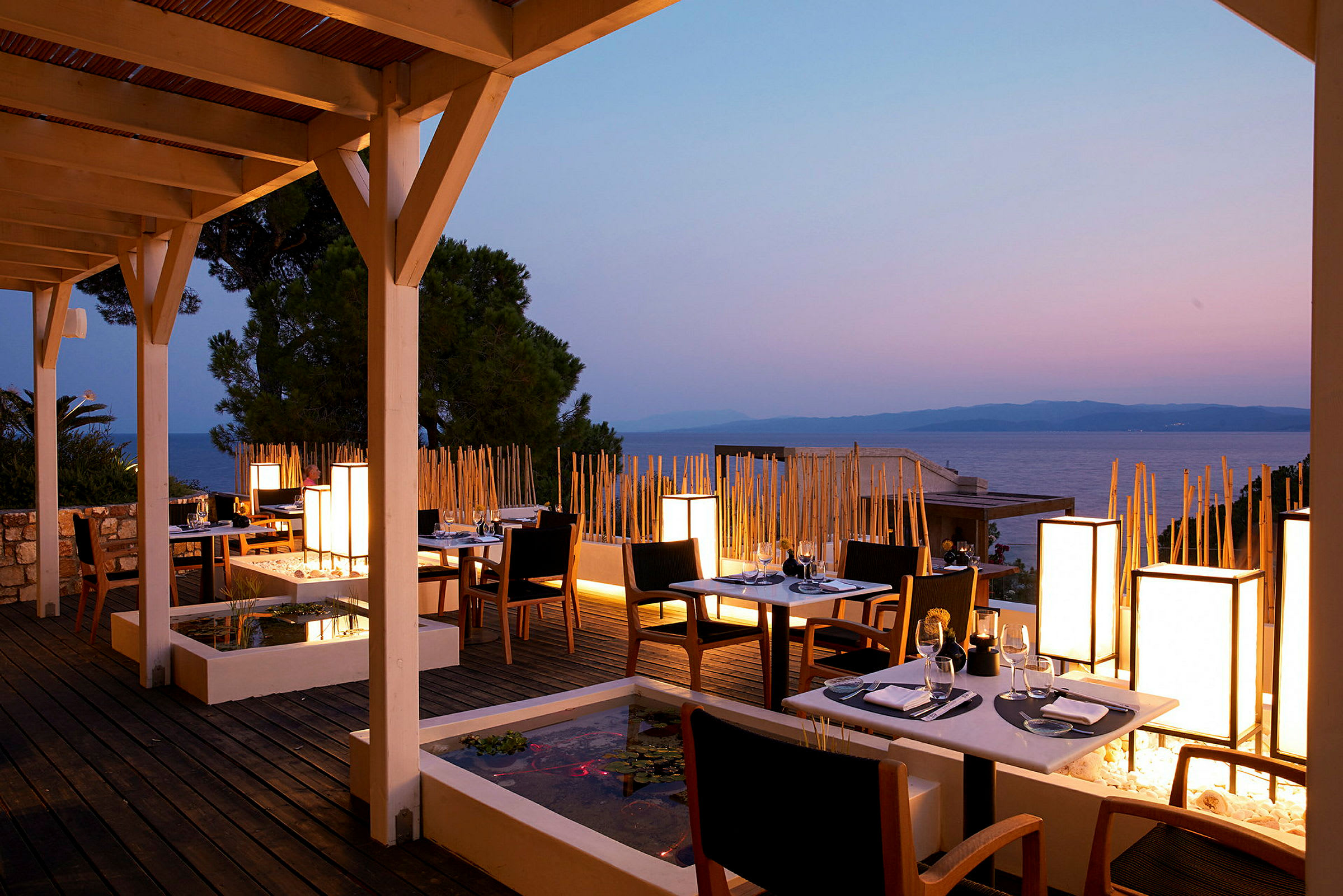 En restaurantterrasse med borde og stole ved solnedgang, havet i baggrunden. (AI-genereret tekst)
