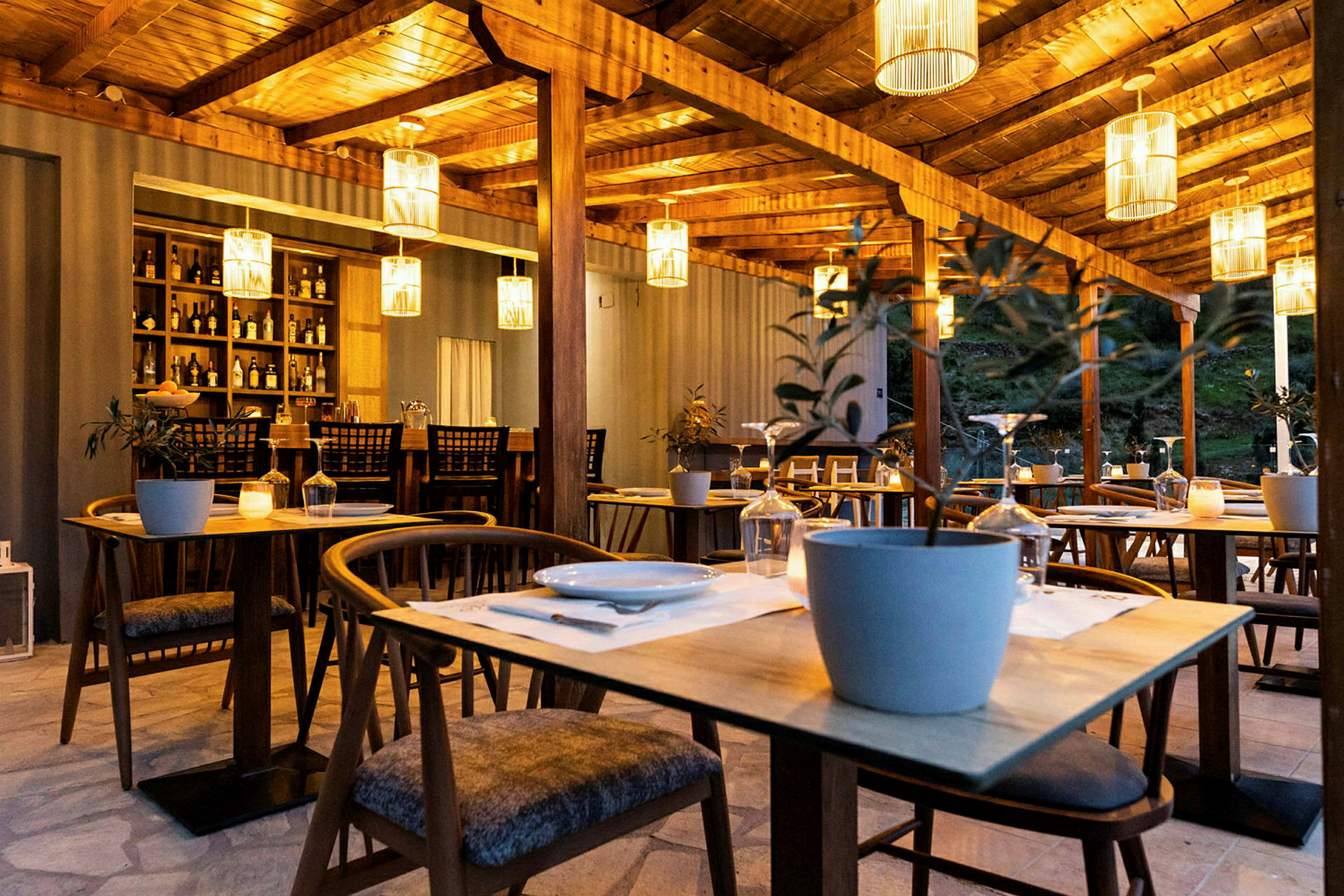En udendørs restaurant med træborde og stole, dekoreret med hængende lampeskærme og potteplanter. (AI-genereret tekst)
