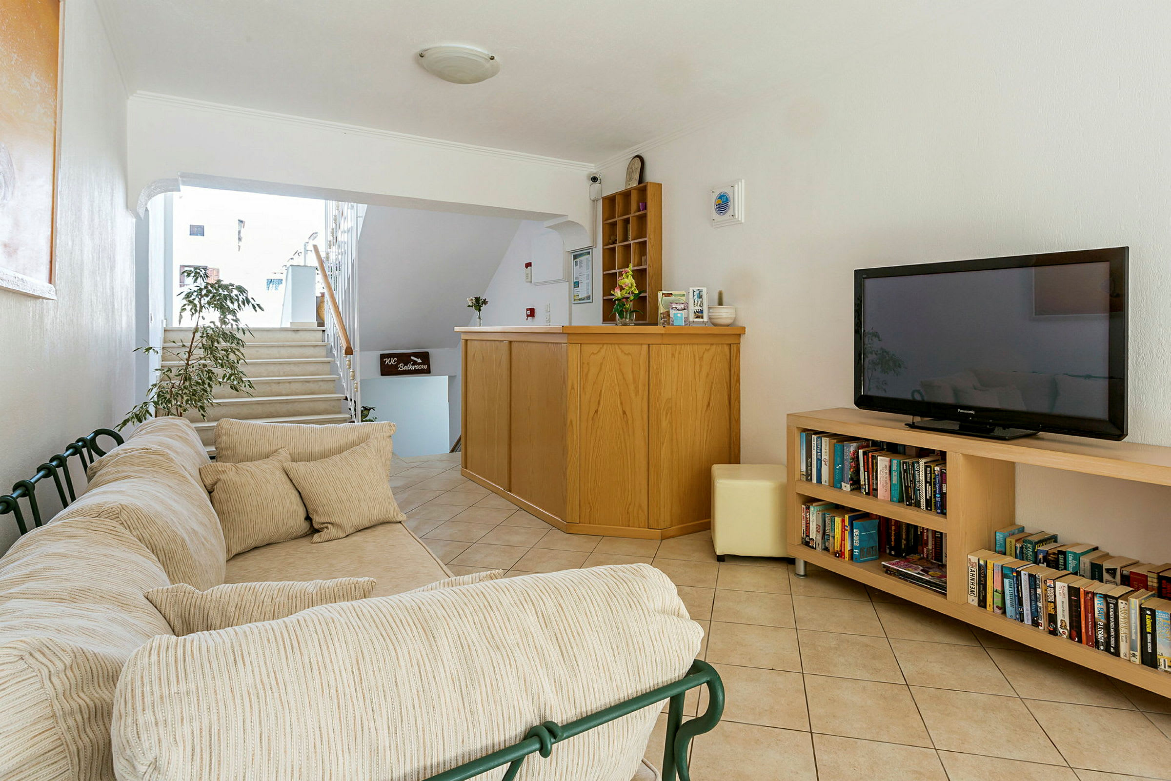 Sofa med puder, reception med skranke og hylde samt boghylde med bøger og TV. (AI-genereret tekst)
