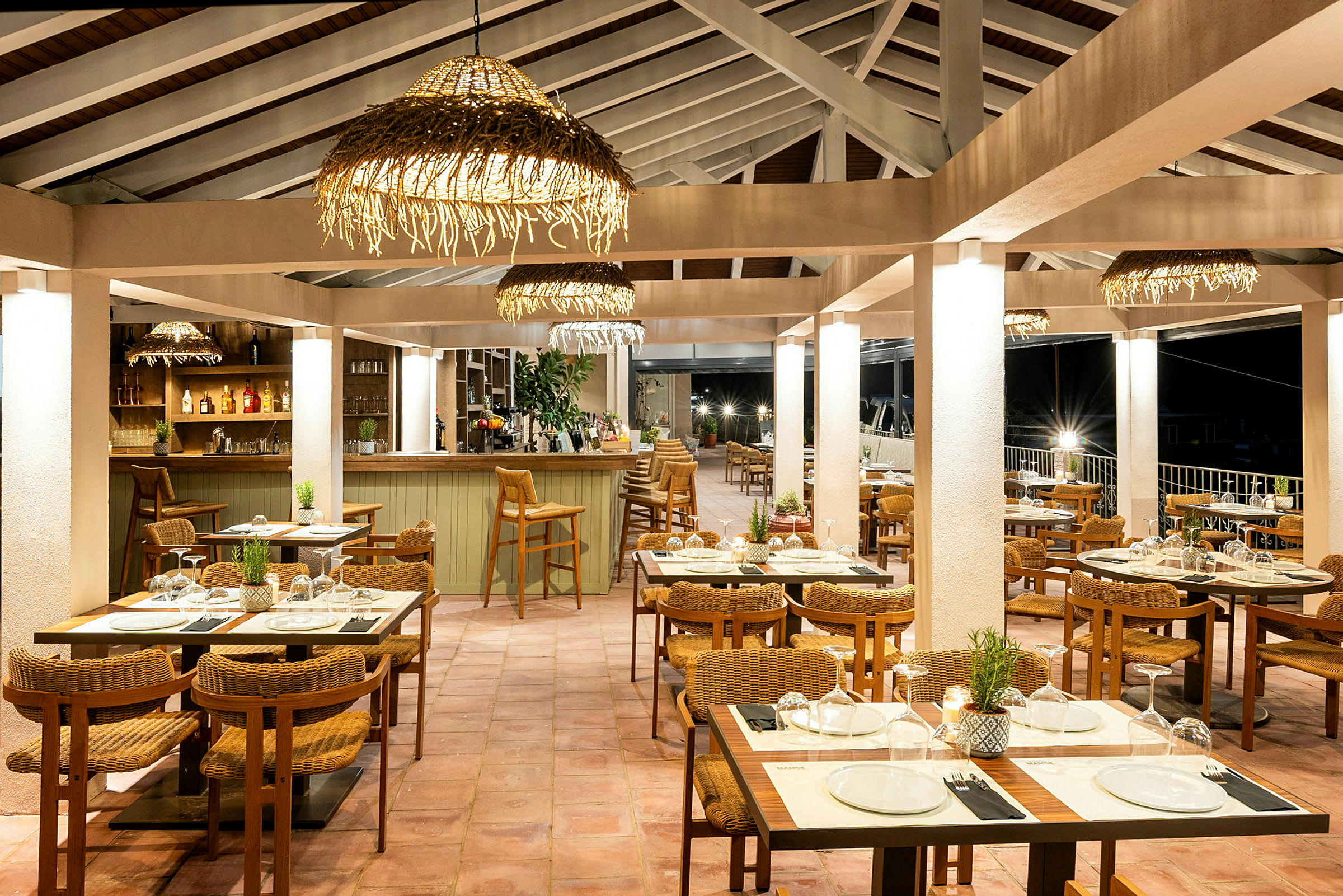 En restaurant med borde og stole samt en bardisk, oplyst med hængende dekorative lamper. (AI-genereret tekst)
