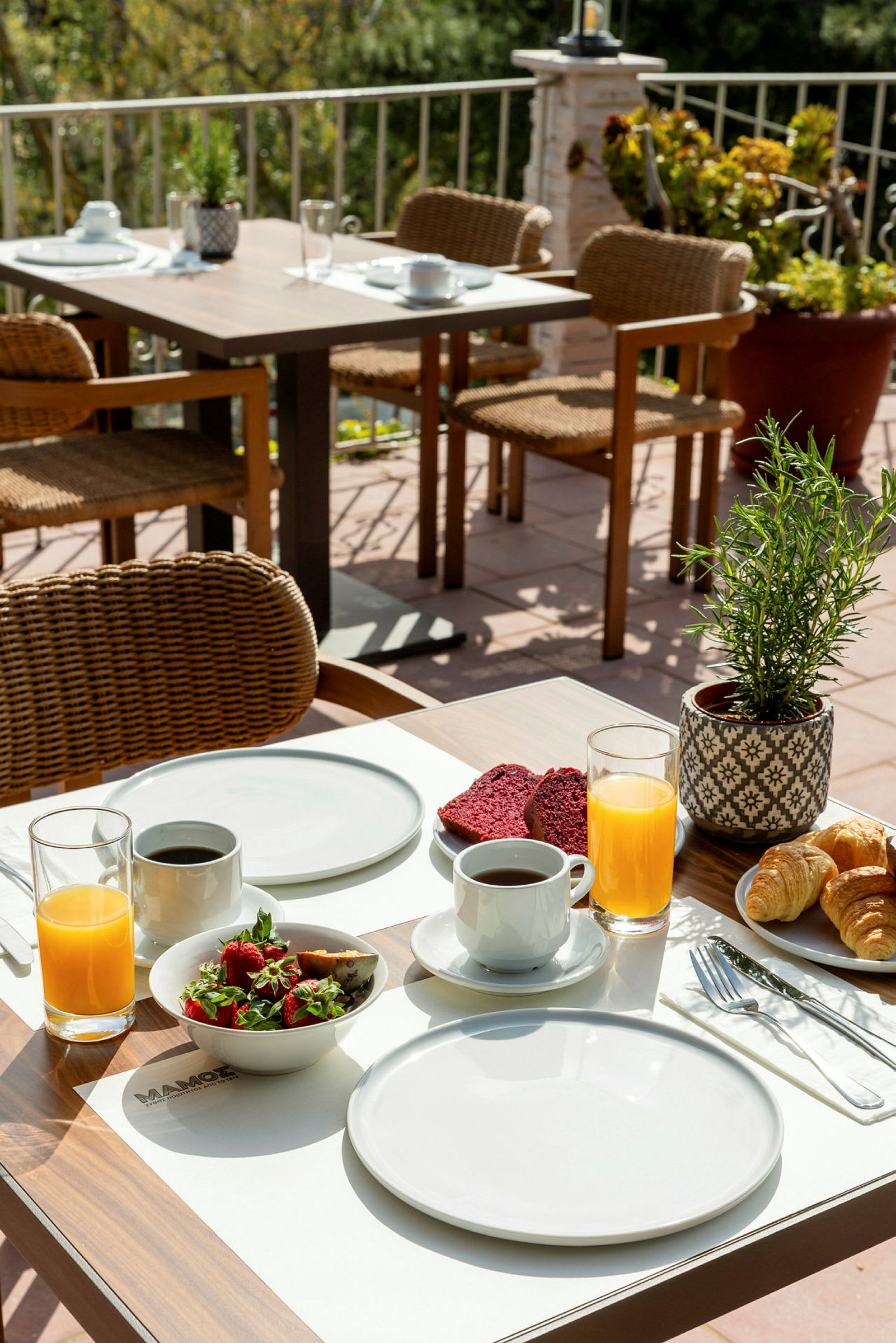 Et dækket bord med morgenmadsbestik, kaffe, juice og morgenmadsretter på en terrasse. (AI-genereret tekst)