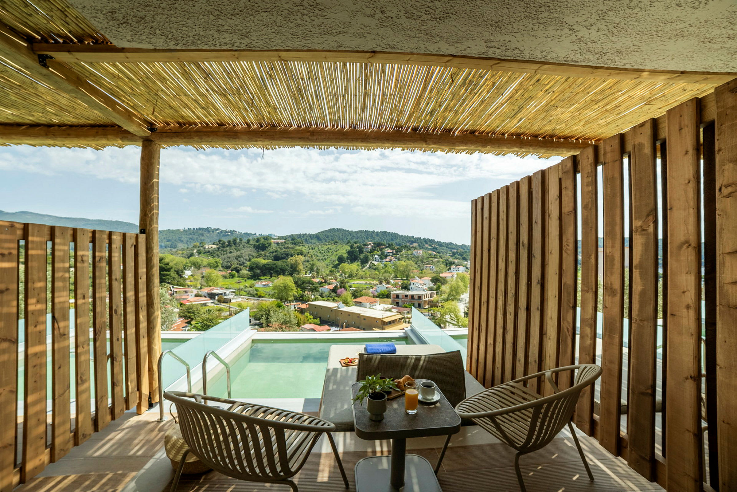 Terrasse med trævægge, bord og stole, pool og udsigt over landskab med huse og grønne bakker. (AI-genereret tekst)
