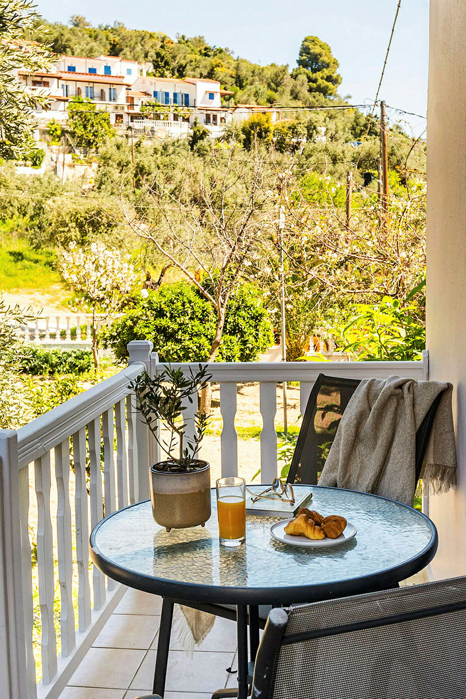 En terrasse med et glasbord, dækket med appelsinjuice og en croissant. (AI-genereret tekst)