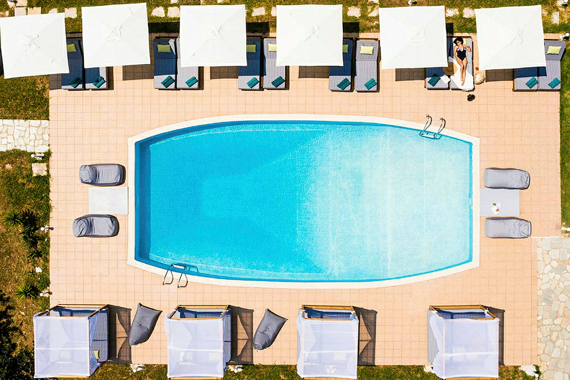 En rektangulær pool omgivet af solsenge med parasoller set ovenfra. (AI-genereret tekst)