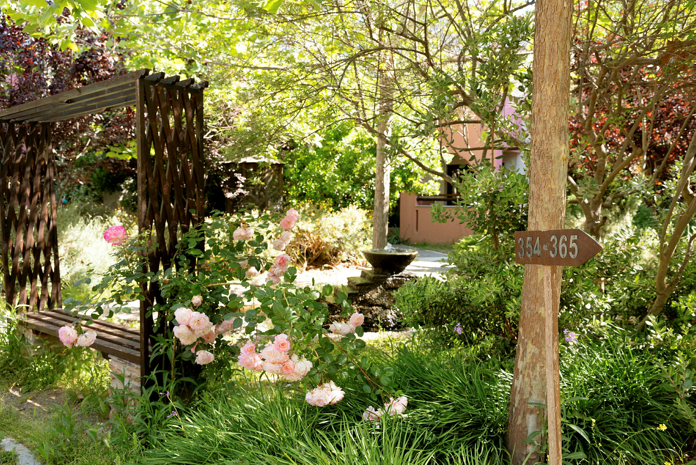 En have med en træbænk, blomster og en fontæne. Et træskilt viser numrene 354-365. (AI-genereret tekst)