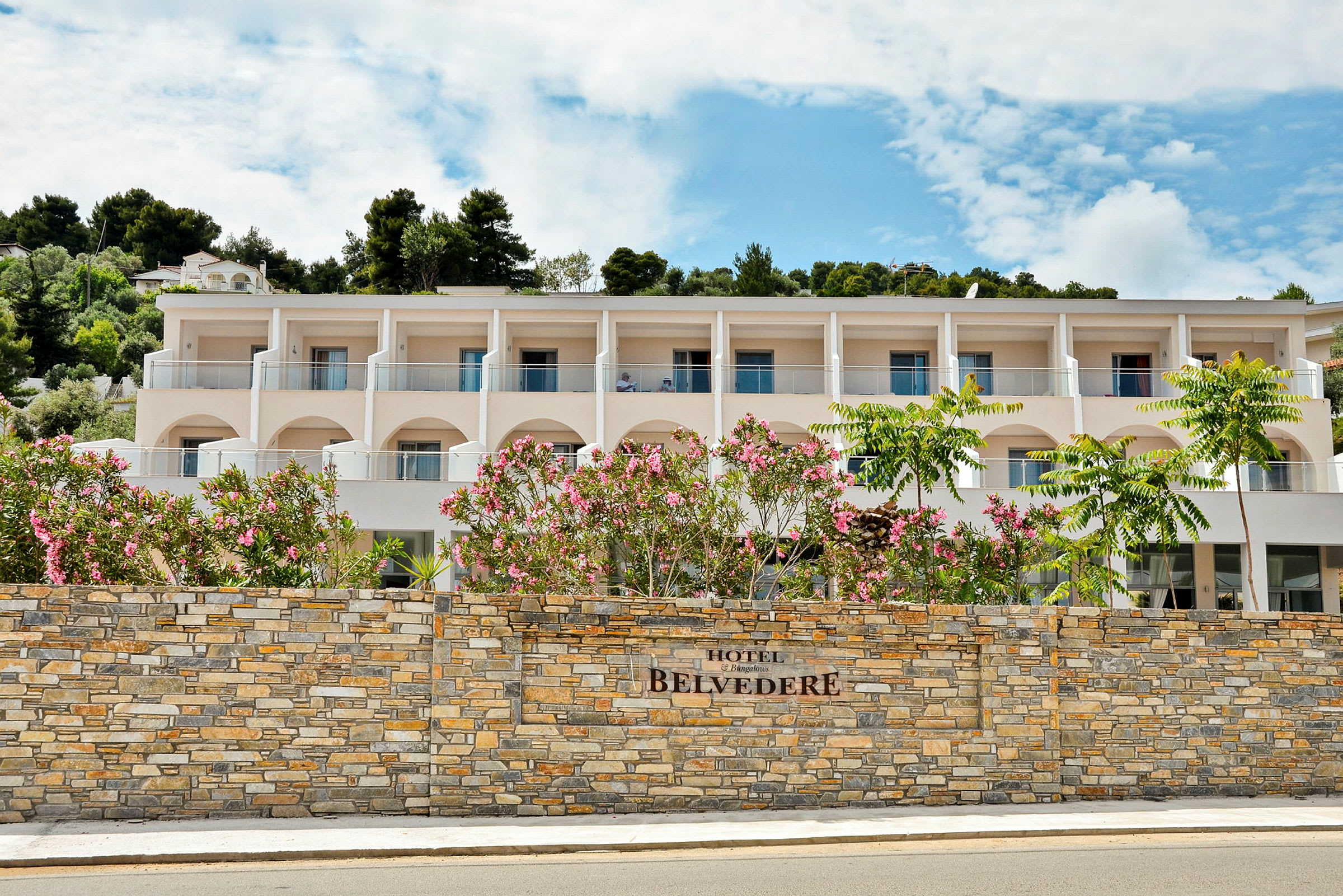 Hotellets facade med altaner og en mur foran samt blomstrende buske. (AI-genereret tekst)