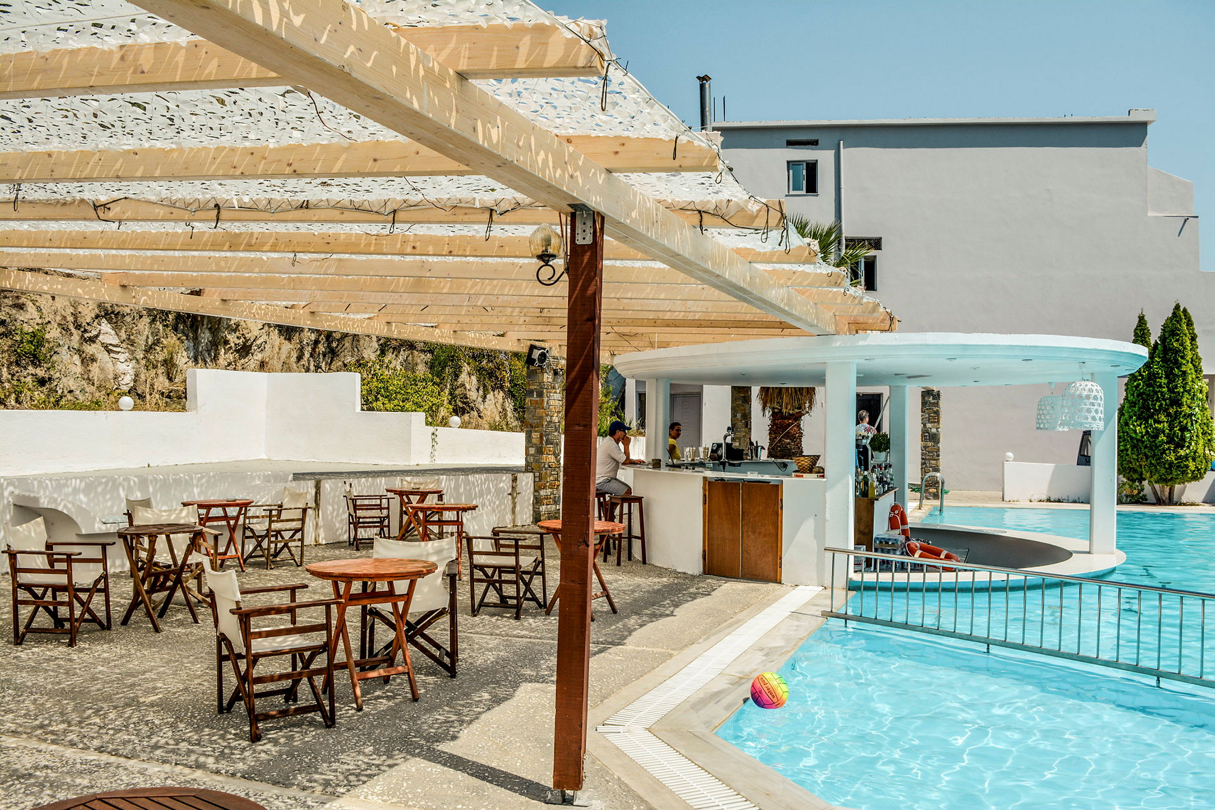Udendørs poolområde med en bar og flere borde og stole under en pergola af træ. (AI-genereret tekst)