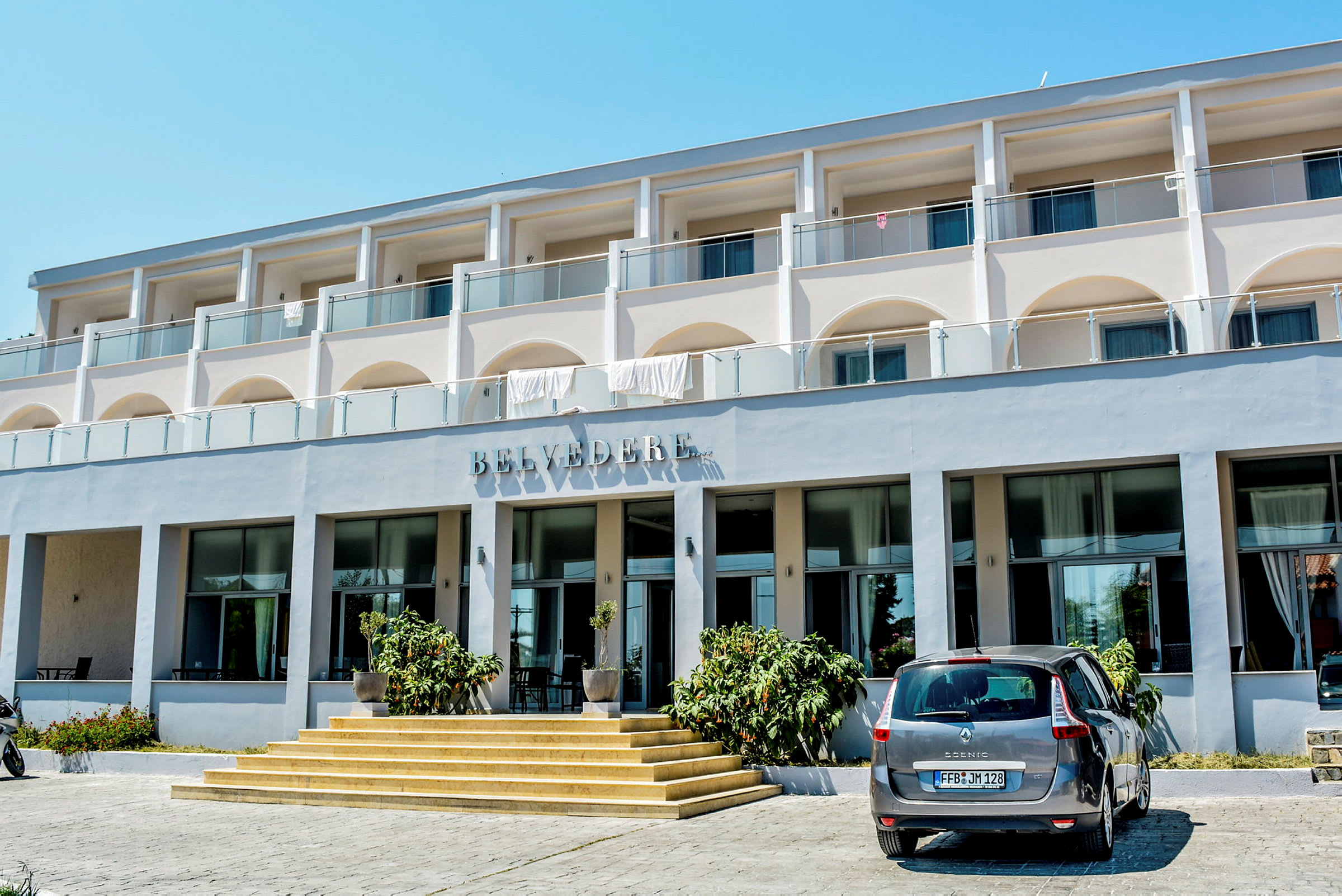 Udvendig af hotelbygningen Belvedere med en bil parkeret foran indgangen. (AI-genereret tekst)