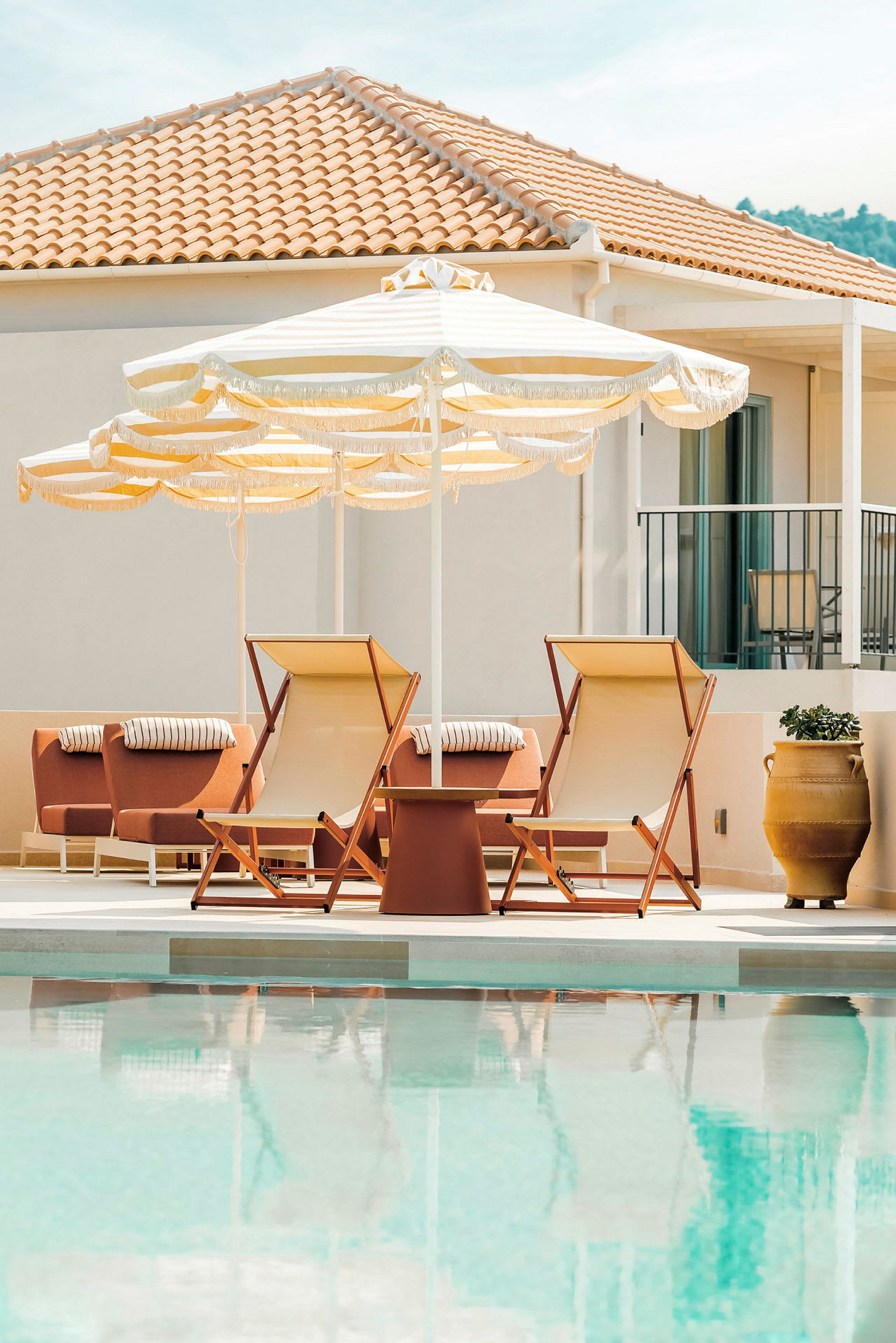 Liggestole og parasoller ved kanten af en udendørs pool, med en bygning med tag i baggrunden. (AI-genereret tekst)