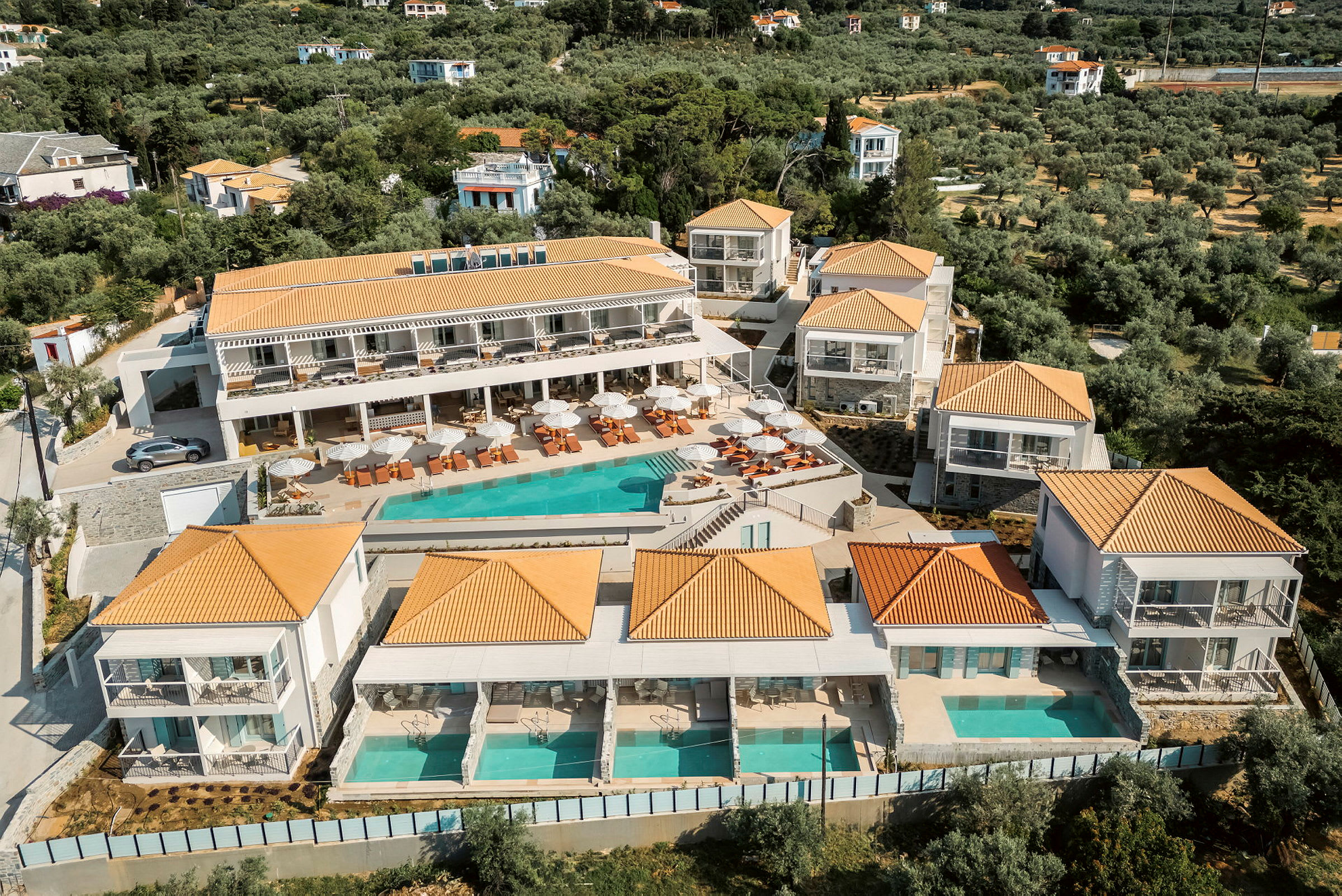 Hotelanlæg med pool og solsenge, omgivet af grønt område. (AI-genereret tekst)