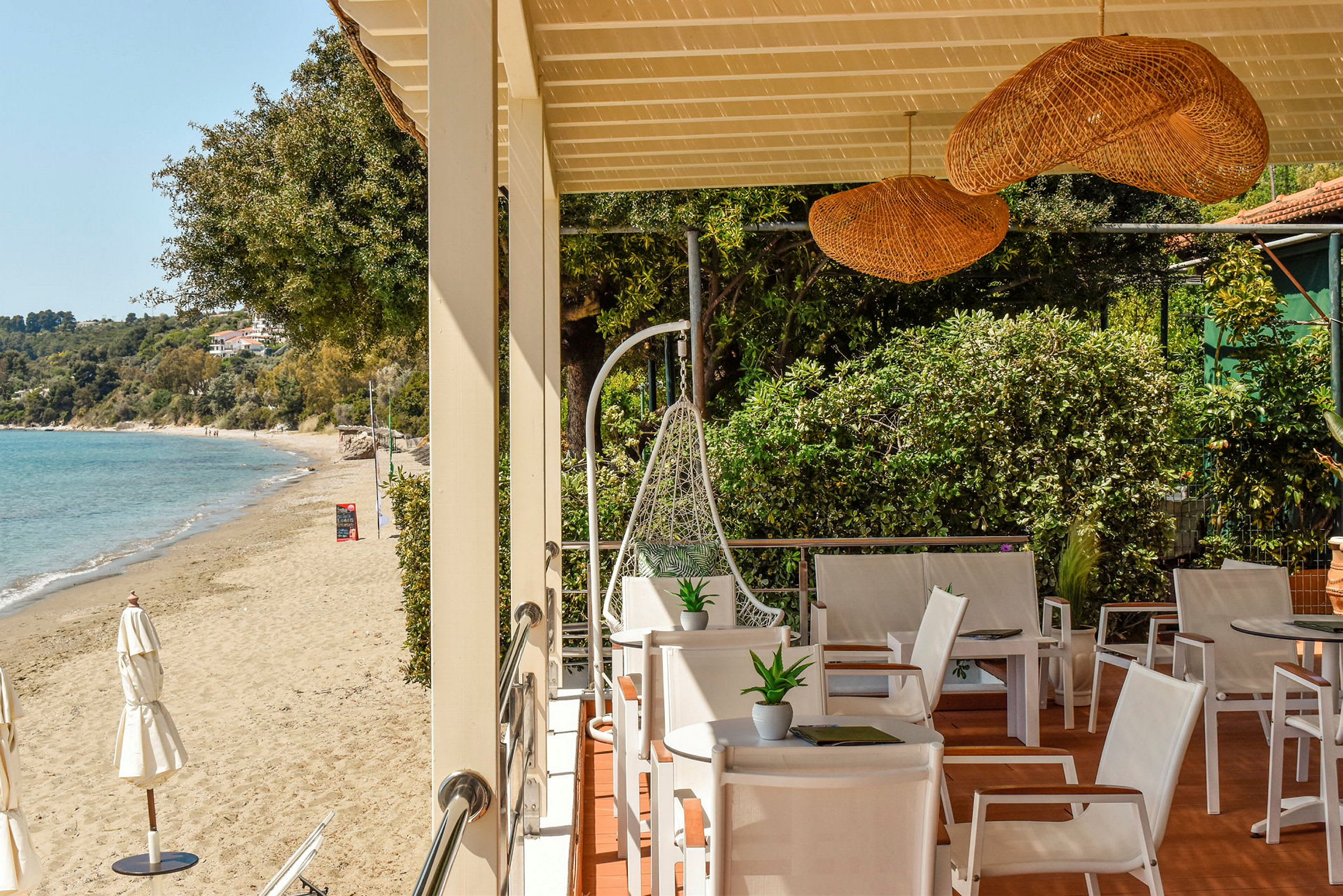 Terrasse med hvide stole og udsigt til en sandstrand og blåt hav. (AI-genereret tekst)