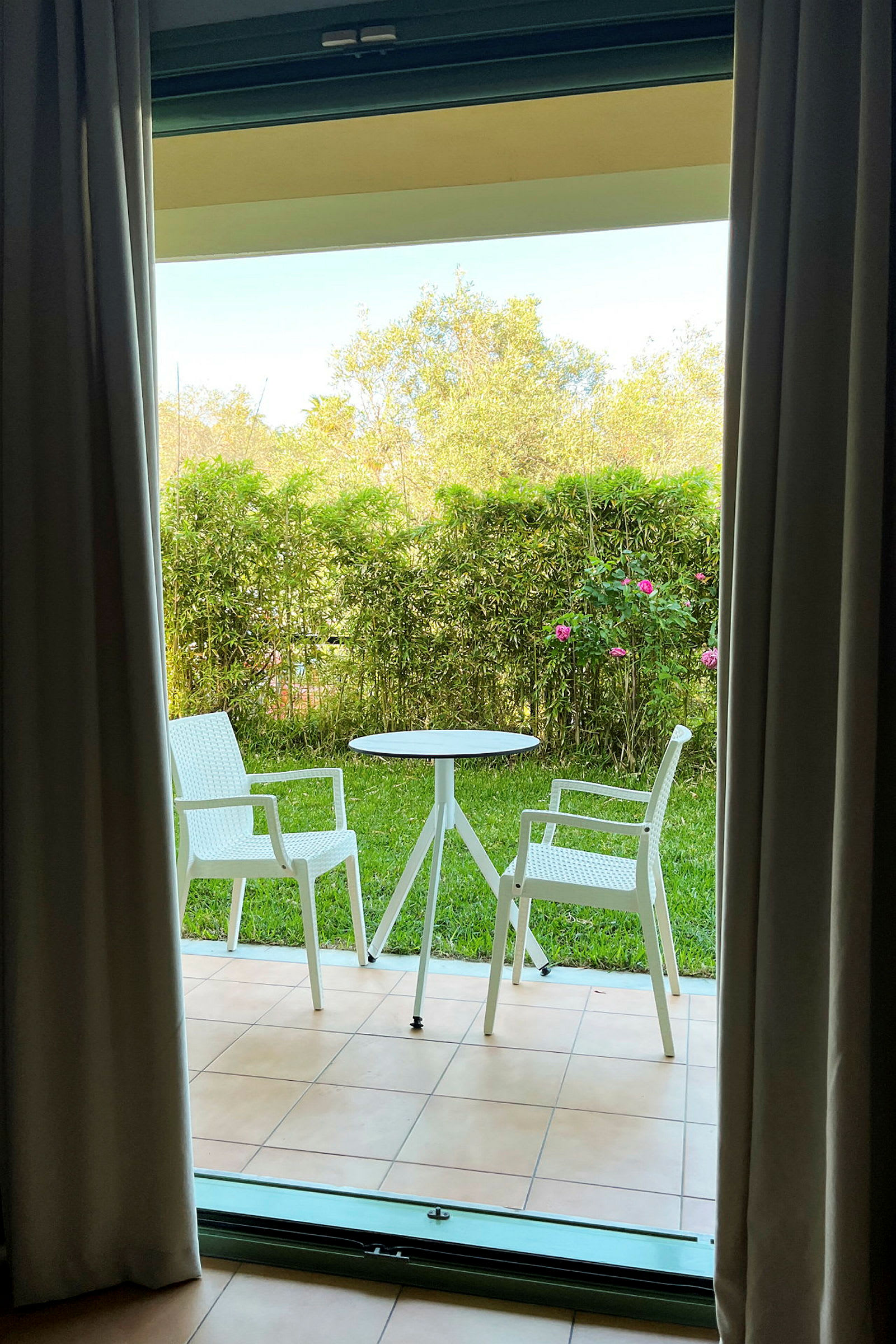 En terrasse med to hvide stole og et bord foran en græsplæne og buske. (AI-genereret tekst)
