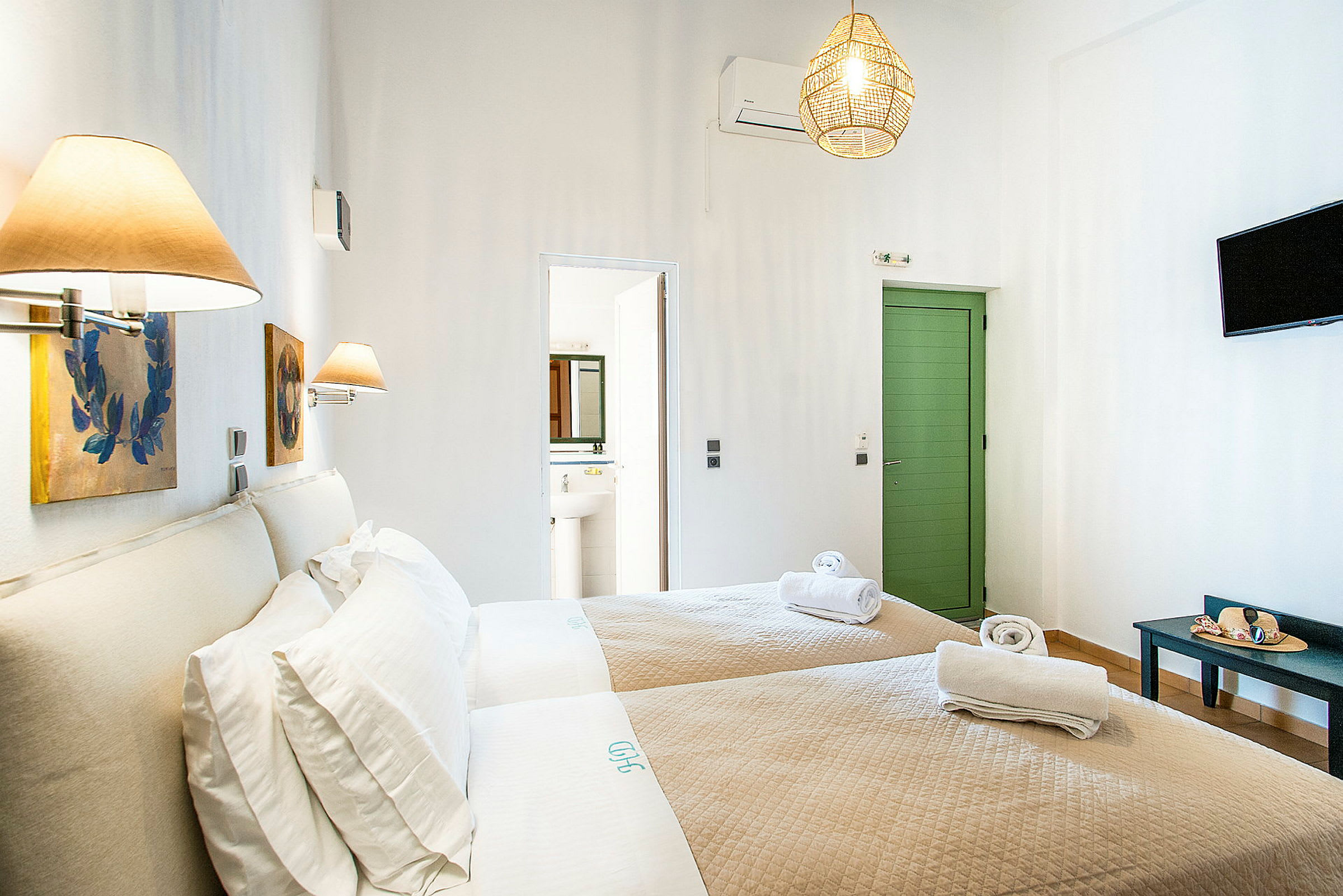 Hotelværelse med to enkeltsenge og beige sengetøj, dekoreret med væglamper og malerier. En dør fører til badeværelset. (AI-genereret tekst)