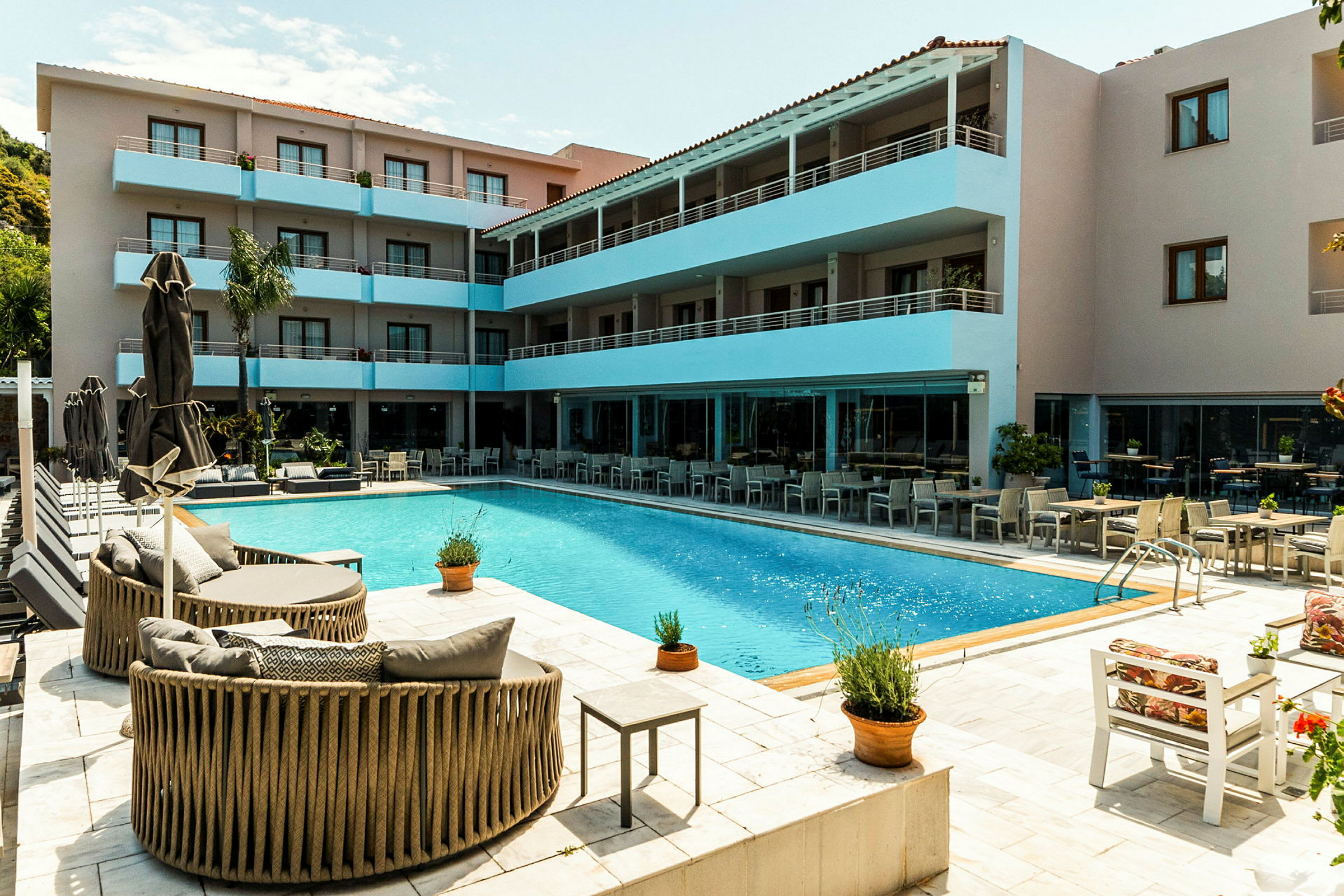 Billede af et hotelområde med en pool, omgivet af siddepladser og en fleretagers bygning med altaner. (AI-genereret tekst)
