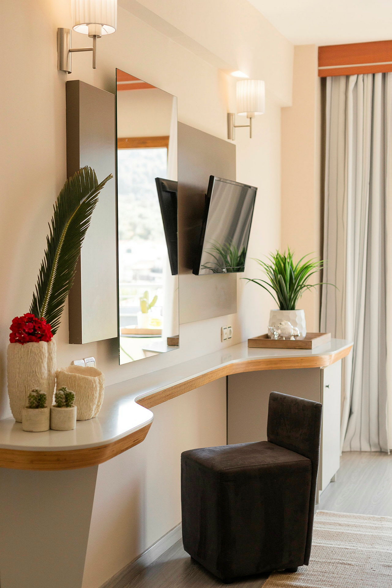 Et moderne hotelværelse med skrivebord og spejl, en lille stol og dekorative planter. (AI-genereret tekst)